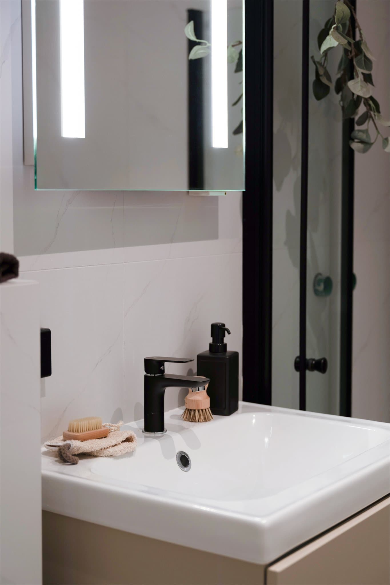 Baderommet er utstyrt med moderne, sorte armaturer og speil med integrert belysning.