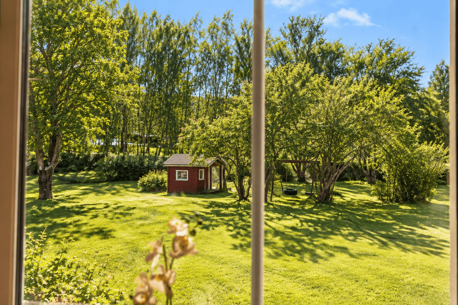 Leiligheten ligger i en høy førsteetasje, tilbaketrukket og med utsyn mot hagen. Bildet er redigert med hjelp av kunstig intelligens fra vinter til sommerbilde.