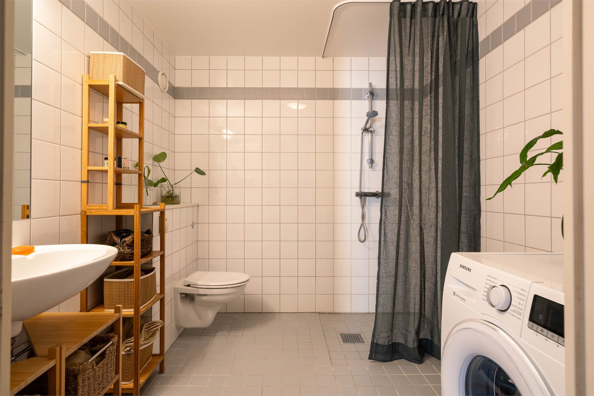 Badet er helflislagt med lyse veggfliser og grå fliser på gulvet.