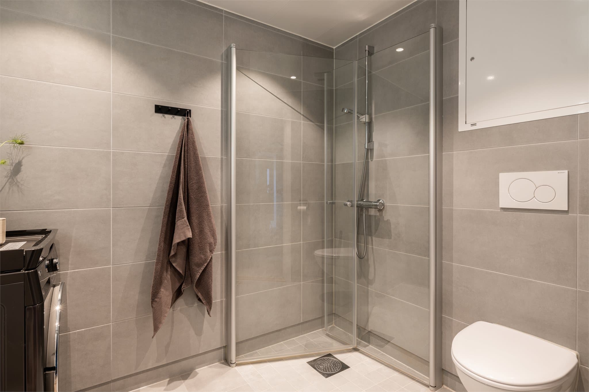 Romslig dusjplass bak innfellbare dører i herdet glass.