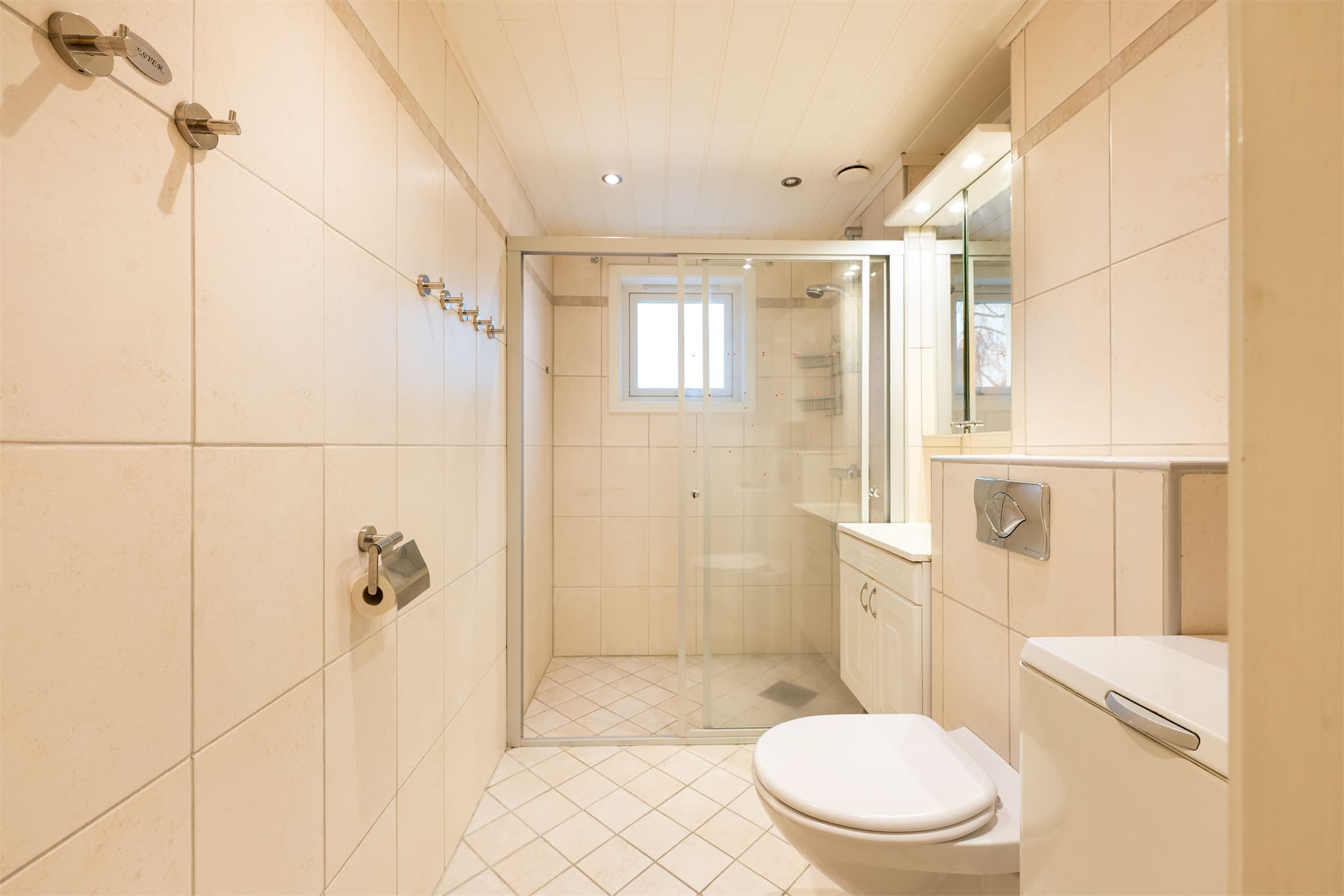 Rommet har servant med profilerte fronter, veggmontert toalett og en romslig dusj.