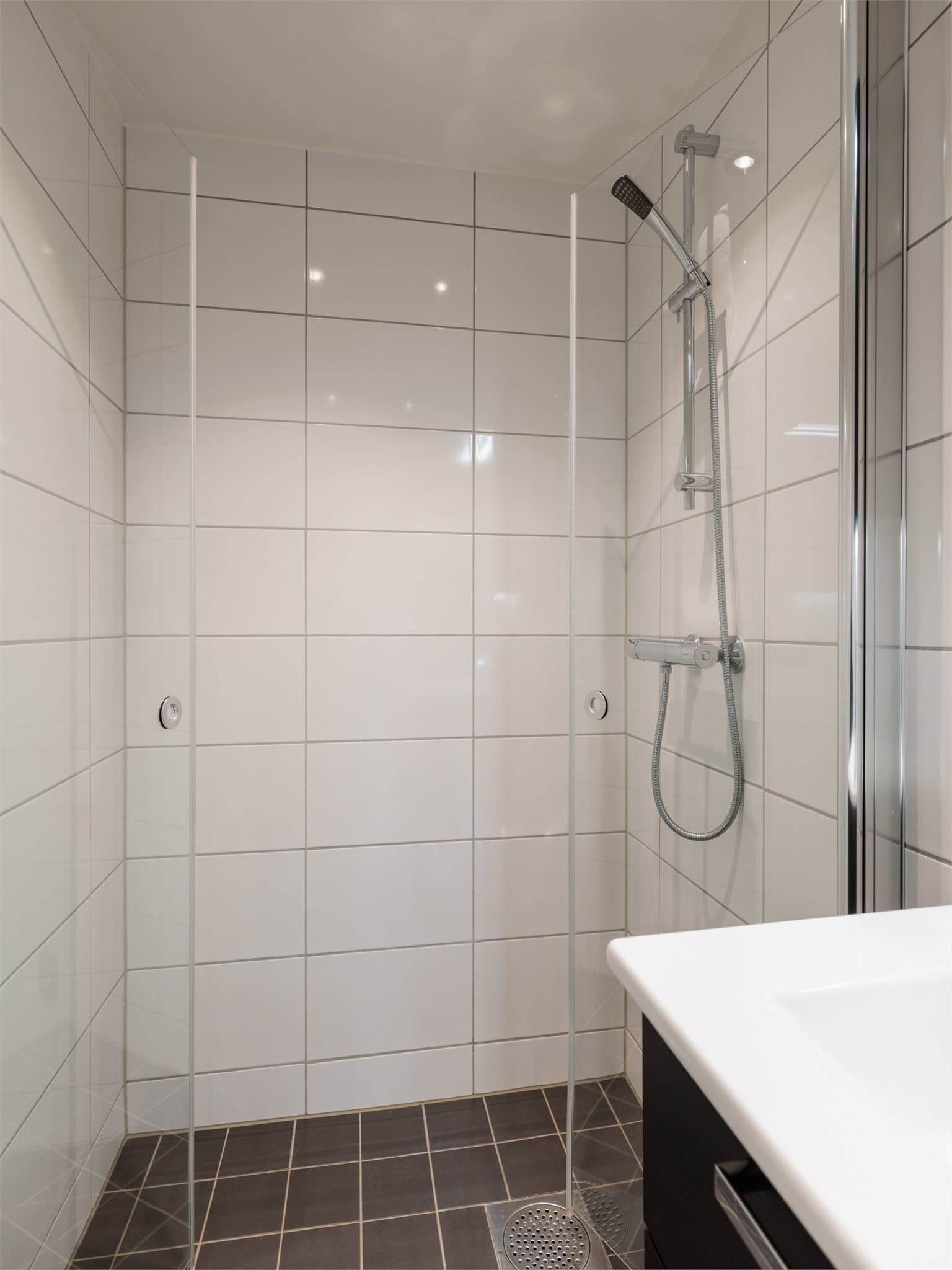 Romslig dusjnisje med innfellbare glassdører og vegghengt toalett.