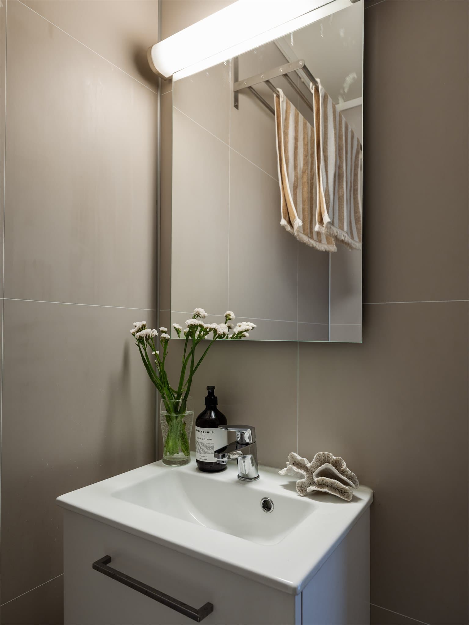 Rommet er utstyrt med elektriske varmekabler i gulv, servant med tilhørende innredning, toalett og dusjhjørne med svingbare glassdører. Veggene er kledd med baderomsplater, og gulvet har vinylbelegg.