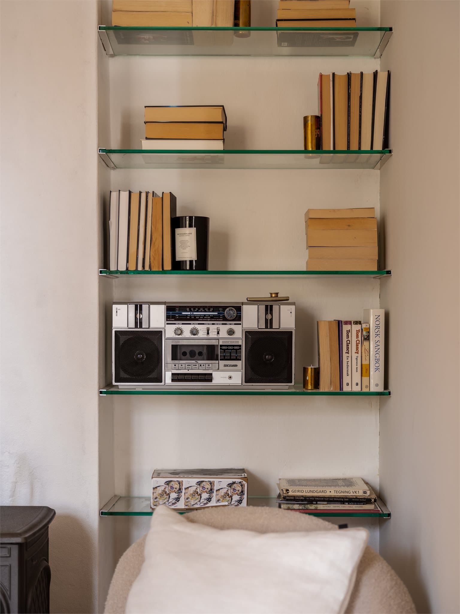 En smart nisje i stuen er utnyttet med plassbygde glasshyller for oppbevaring og dekor.