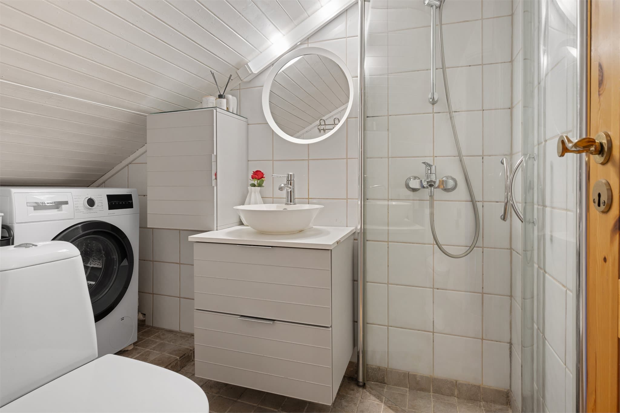 Baderommet har dusjløsning, servant på skuffeseksjon og gulvstående toalett.