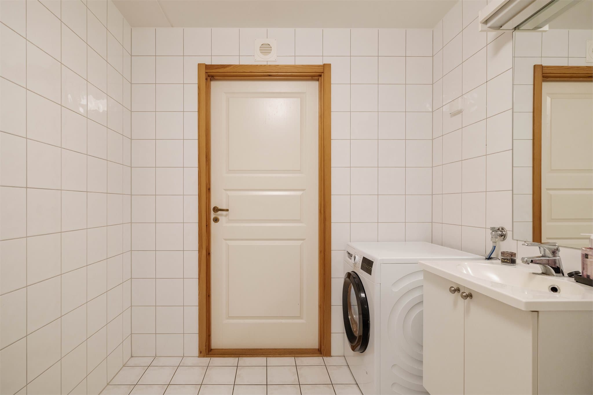 Innredningen på badet består av skap med glatte fronter, servant, toalett, dusj på gulv og opplegg for vaskemaskin.