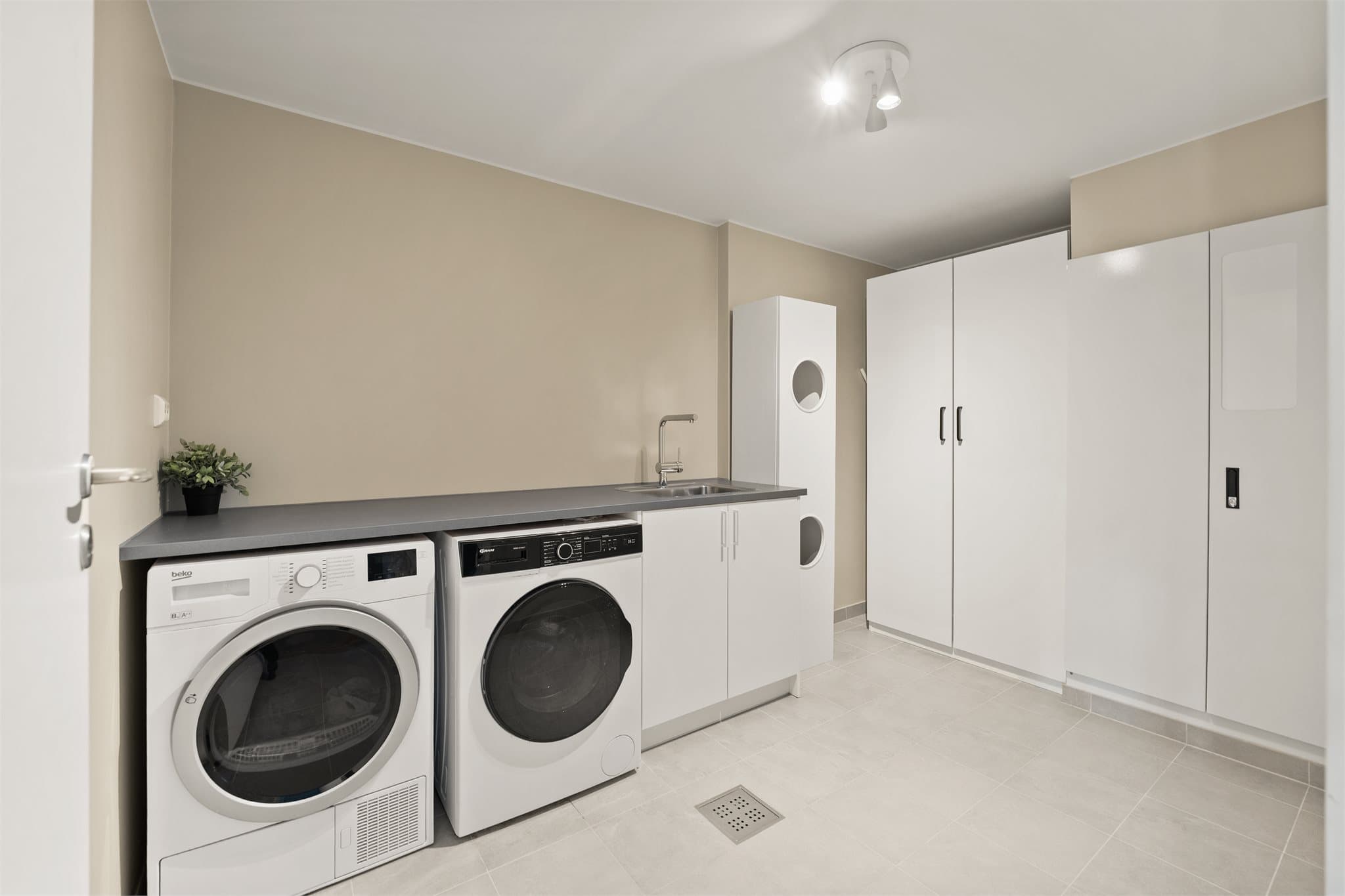 Praktisk vaskerom/teknisk rom med opplegg for vaskemaskin og tørketrommel. Her har man god benkeplass og lagringsmuligheter i skap.