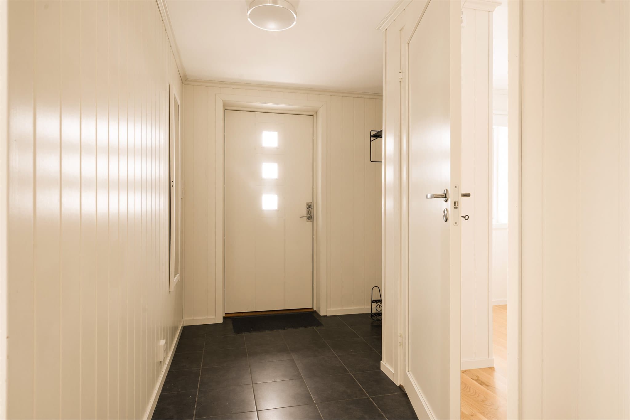 Lysmalt entré med flislagt gulv og gulvvarme. Nisje hvor det er montert knaggrekke.