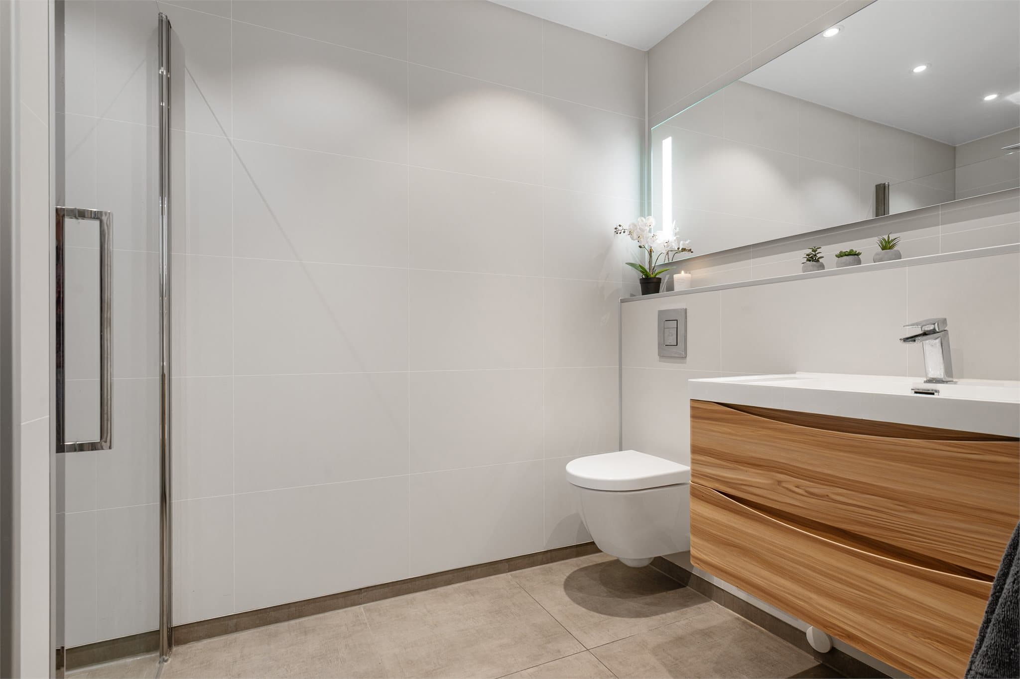 Innredningen består av vegghengt toalett, helservant på skuffeseksjon, speil med belysning og dusjnisje.