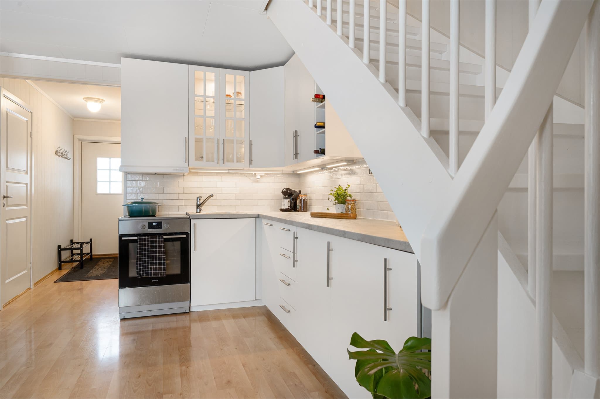 Tidløs kjøkkeninnredning med hvite, slette fronter, vitrineskap og laminat benkeplate.