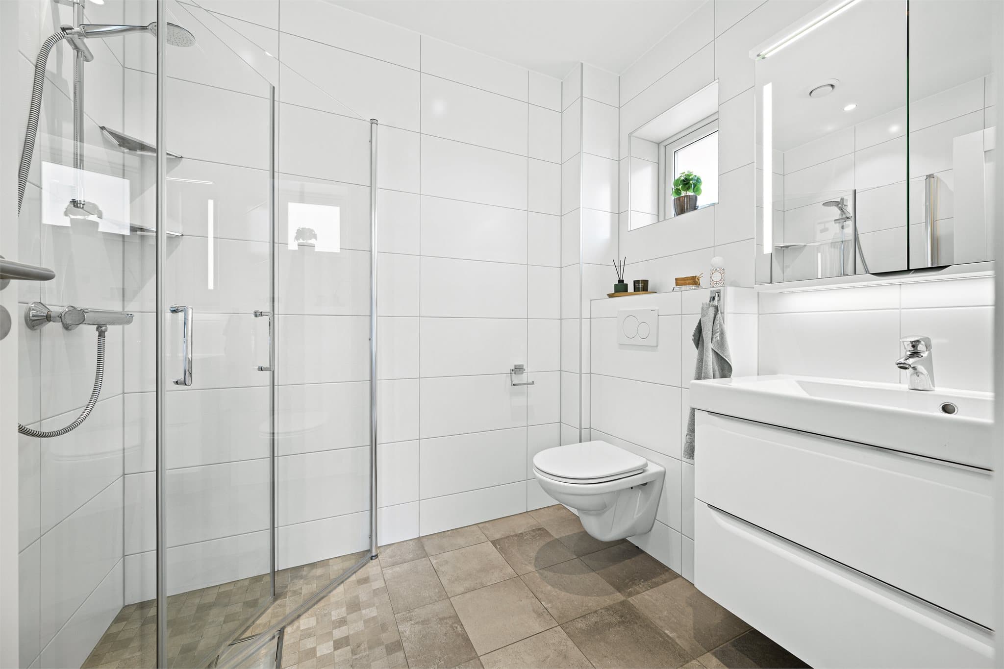 Delikat og stilrent baderom i suiteløsning til hovedsoverommet. Badet er helflislagt i tidløse fargetoner og innredet med romslig dusjhjørne med glassvegger, moderne servantinnredning med gode oppbevaringsmuligheter samt vegghengt toalett.