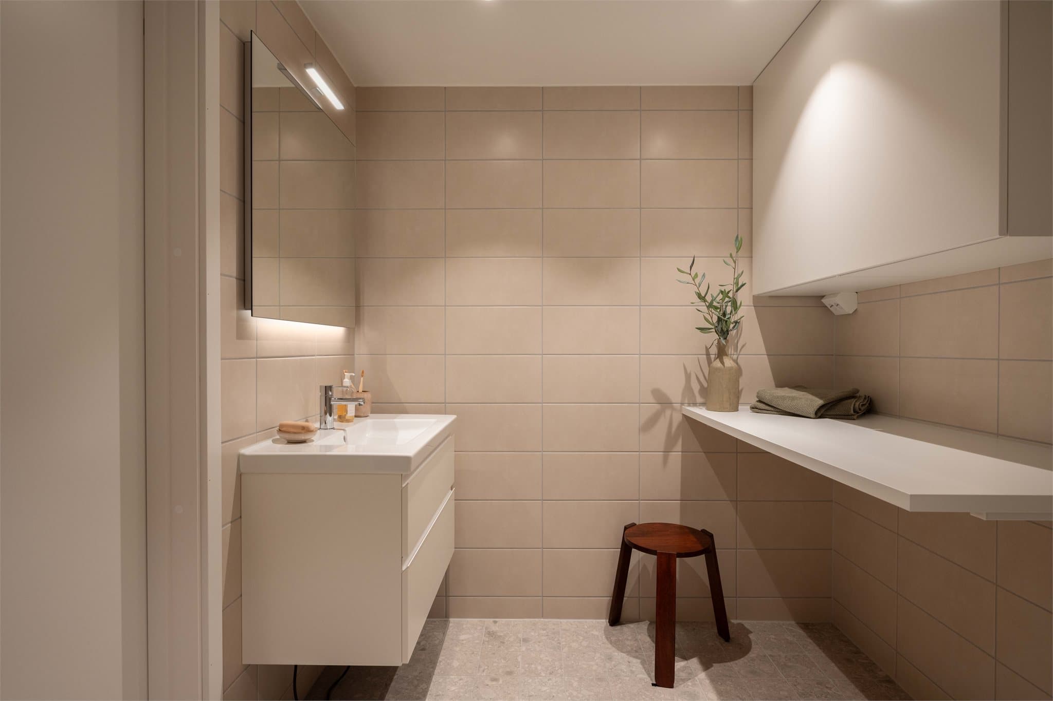 Baderommet har praktisk skap, servantskap og benk for oppbevaring.