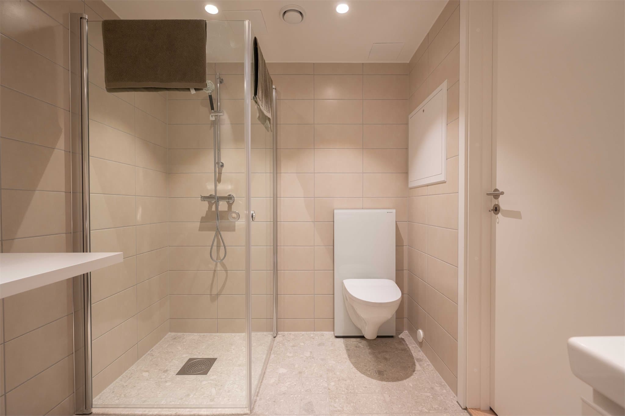 Delikat, flislagt bad med vegghengt toalett og dusjhjørne med innfellbare glassdører.