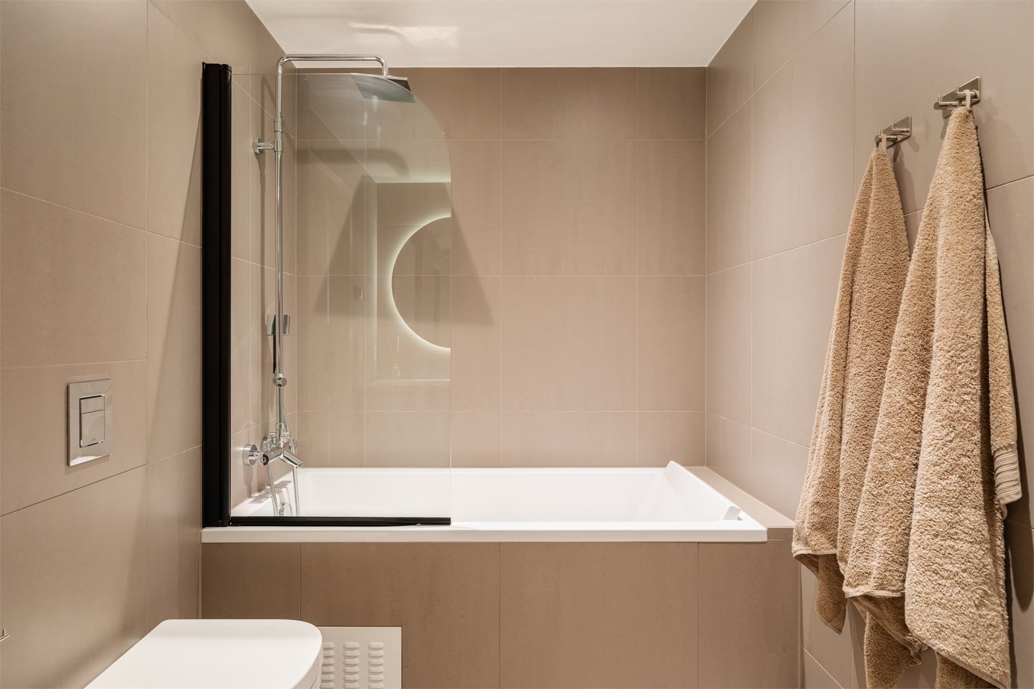 Det andre badet har store, moderne fliser på vegger og gulv og er innredet med innbygget badekar, servantinnredning med profilerte fronter og heldekkende servant, samt toalett.