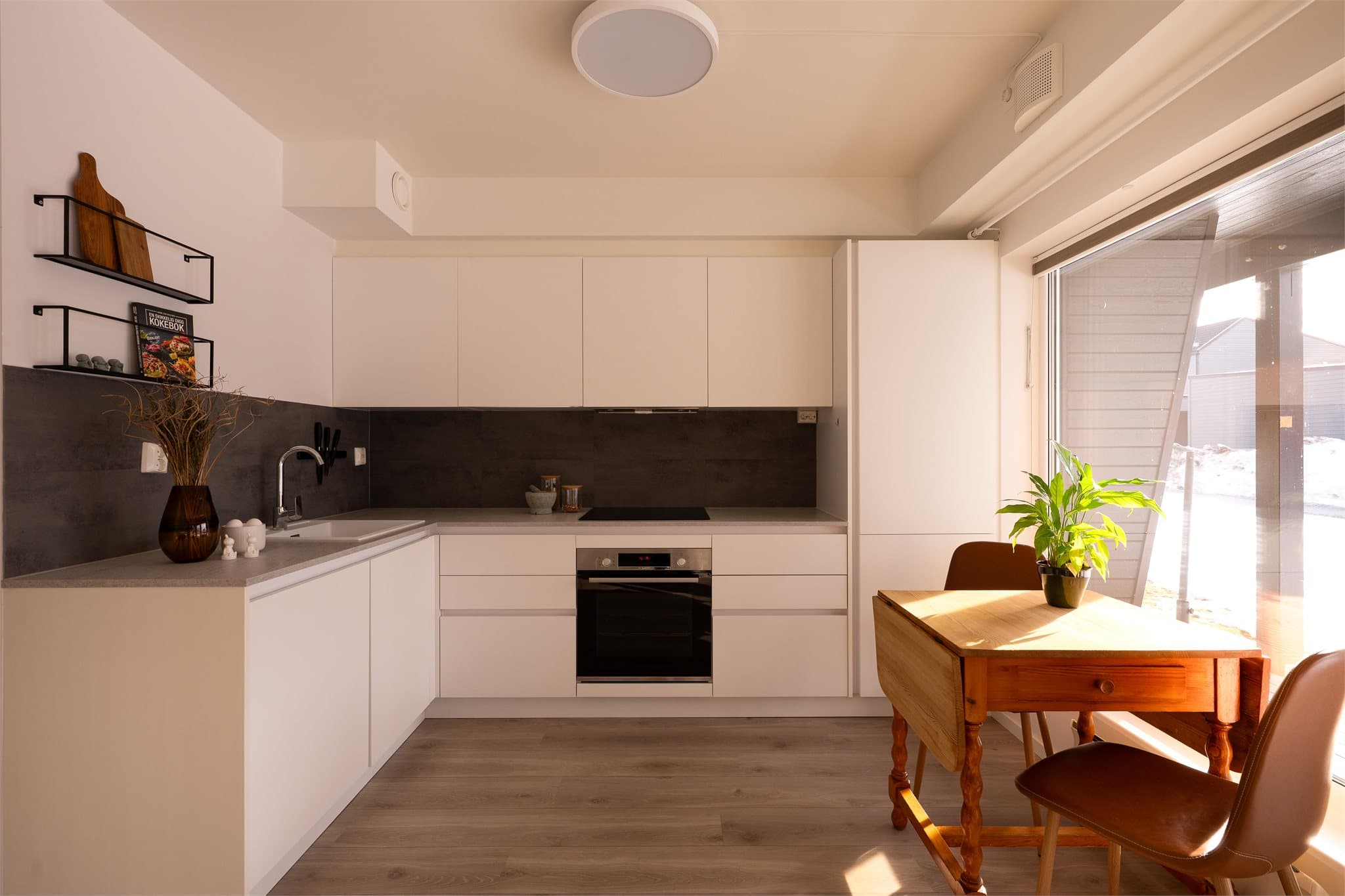 Kjøkkeninnredningen har hvite, slette fronter og laminat benkeplate.