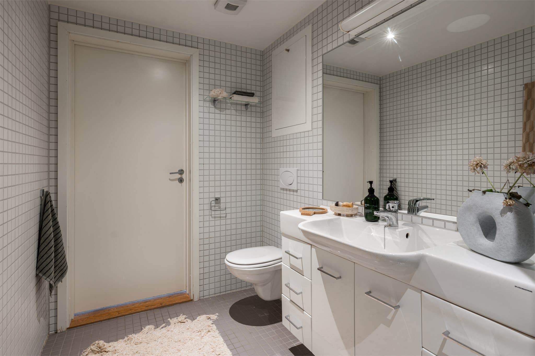 Badet har vegghengt toalett, servant med underskap og opplegg for vaskemaskin.