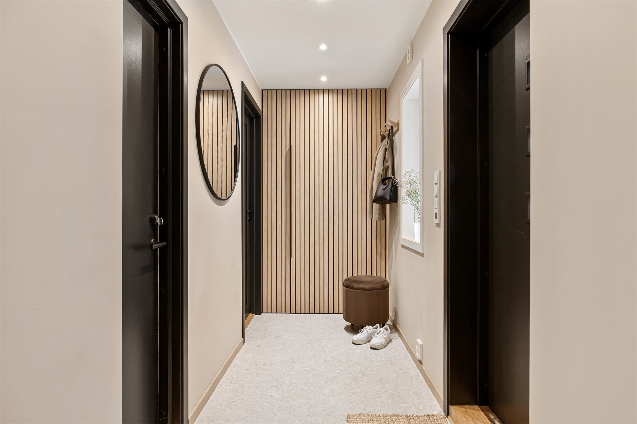 En moderne entré med downlights i tak og smart oppbevaring bak spilevegg.