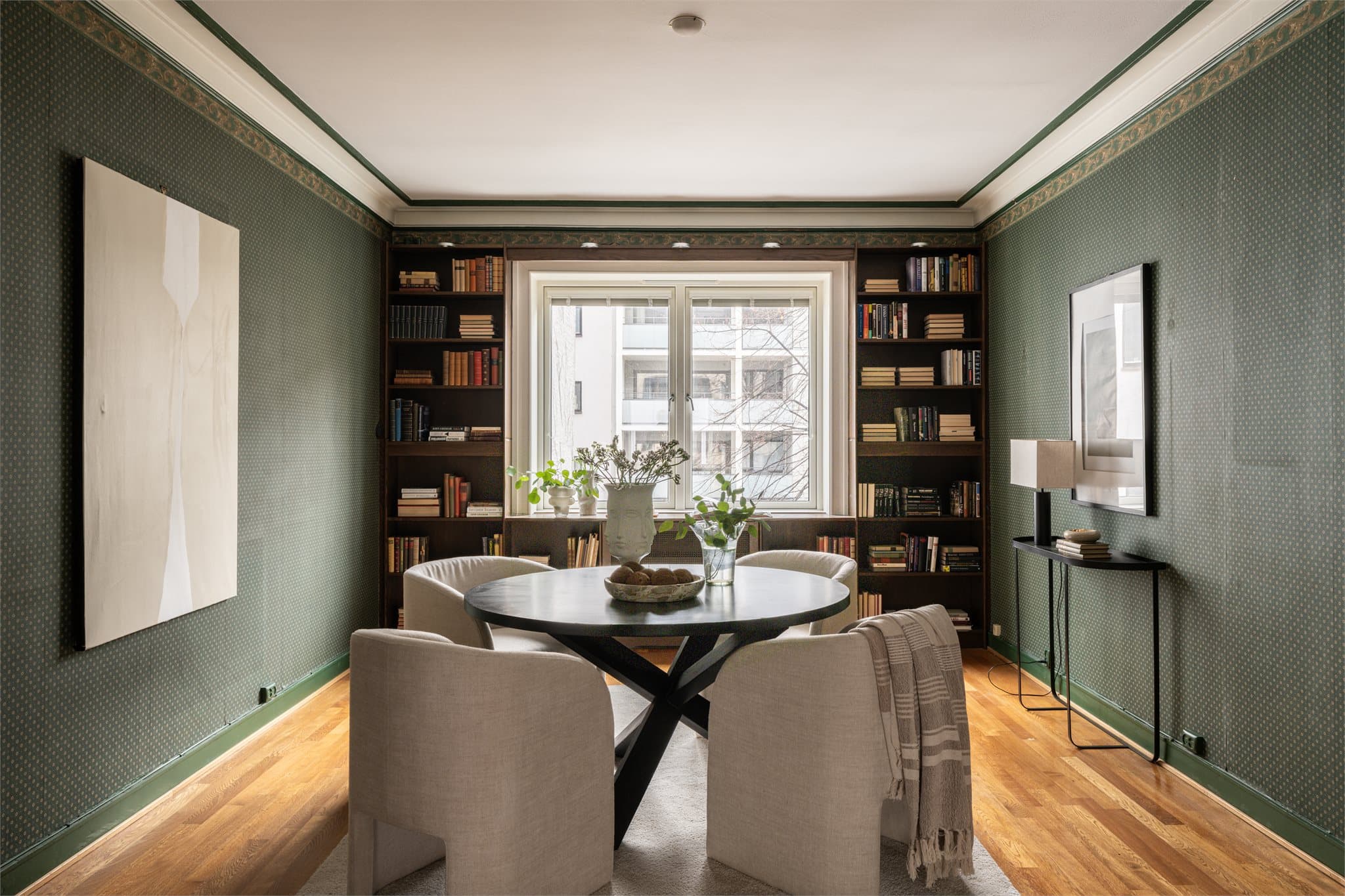 Spisestue med plass til stort spisebord, omgitt av integrerte bokhyller og gode lysforhold fra vinduet.