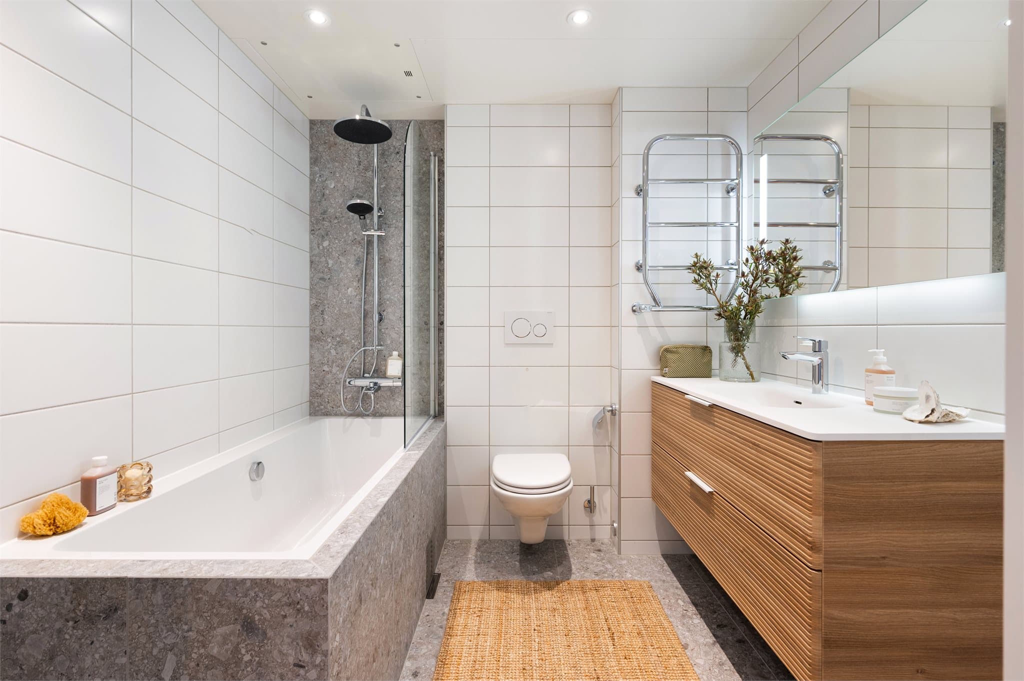 Prefabrikkert baderom med flislagte overflater, vegghengt toalett, dusjhjørne med glassdører og opplegg for vaskemaskin og tørketrommel.