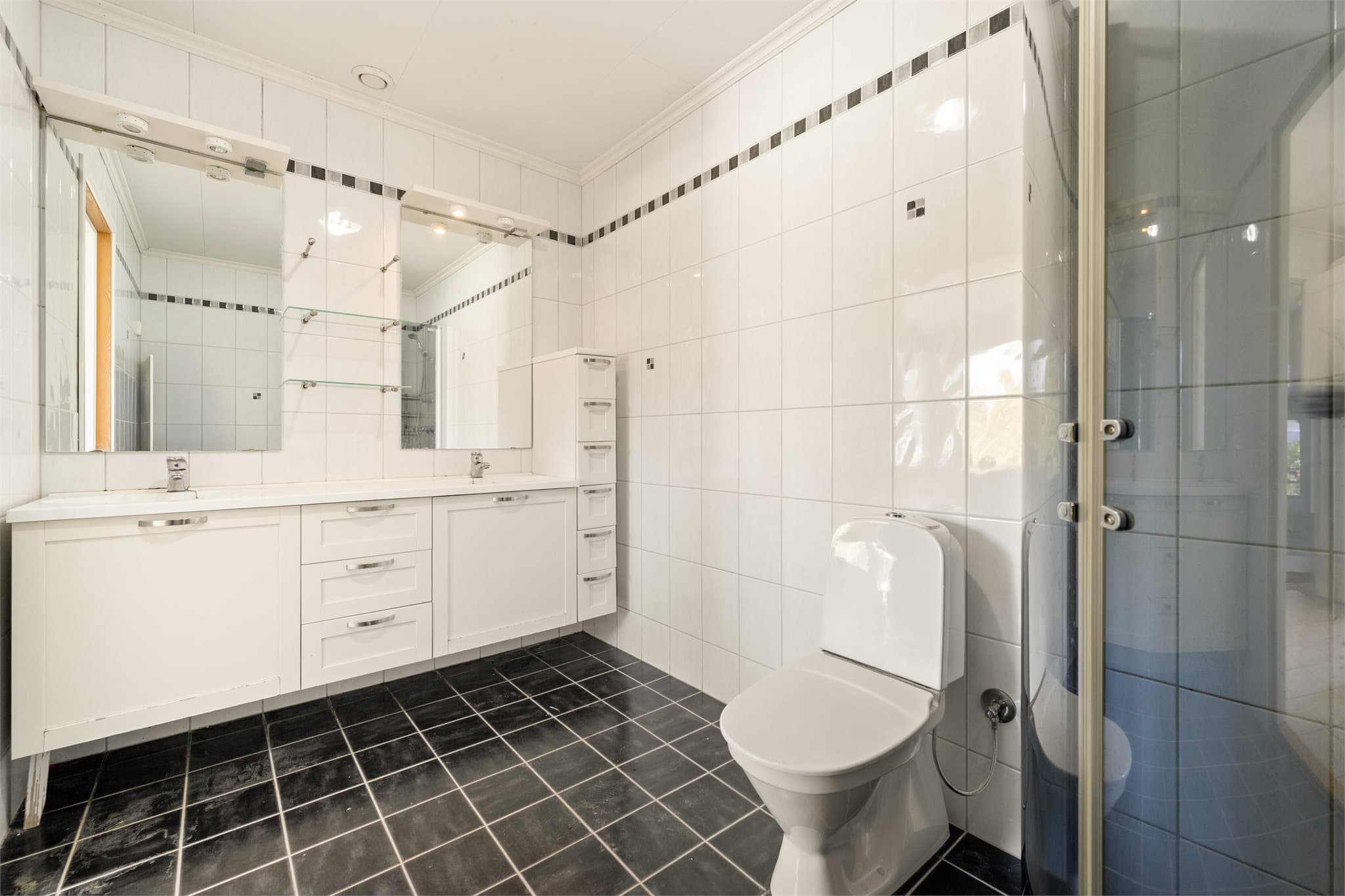 Baderommet fremstår som funksjonelt og romslig, med en tidstypisk stil fra byggeåret 2007. Her er det mørke, kvadratiske fliser på gulv med behagelig gulvvarme som står i fin kontrast til lyse veggfliser, og skaper et klassisk og varig uttrykk.