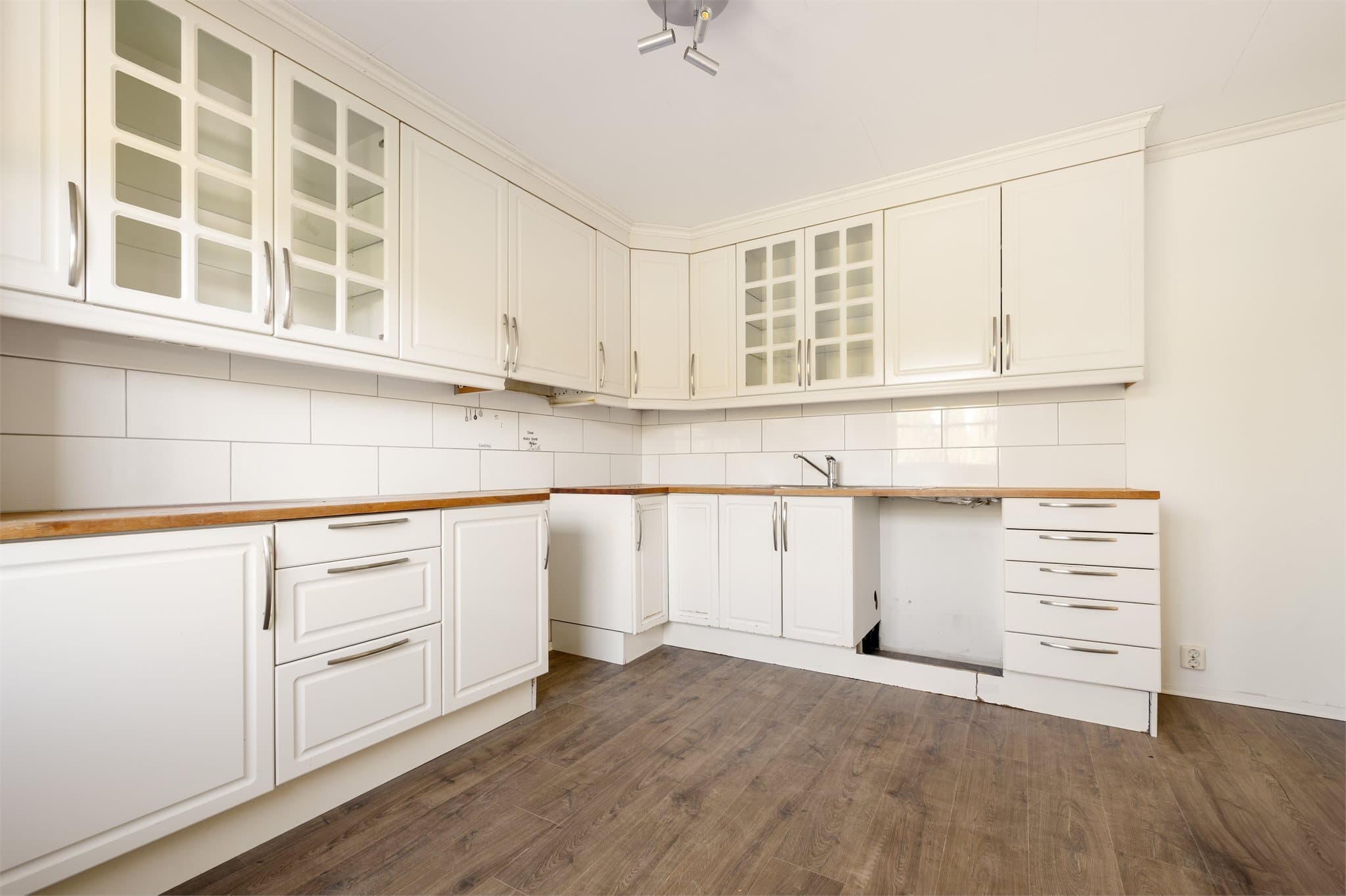 Kjøkkenet ligger i et eget rom og er utformet i en praktisk L-løsning som gir gode arbeidsflater og en effektiv arbeidssone. Her er det avsatt plass til hvitevarer, og fliser mellom benk og overskap gir et både funksjonelt og stilrent uttrykk.