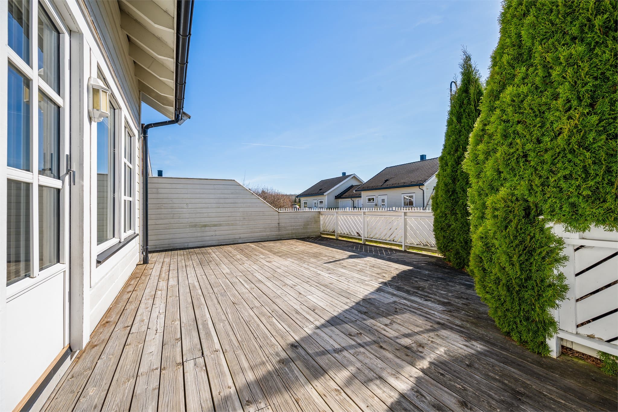 Terrassen leder videre ut til en hyggelig, omkransende hage med hvitt stakittgjerde – perfekt for både lek, avslapning og rolige stunder i grønne omgivelser.