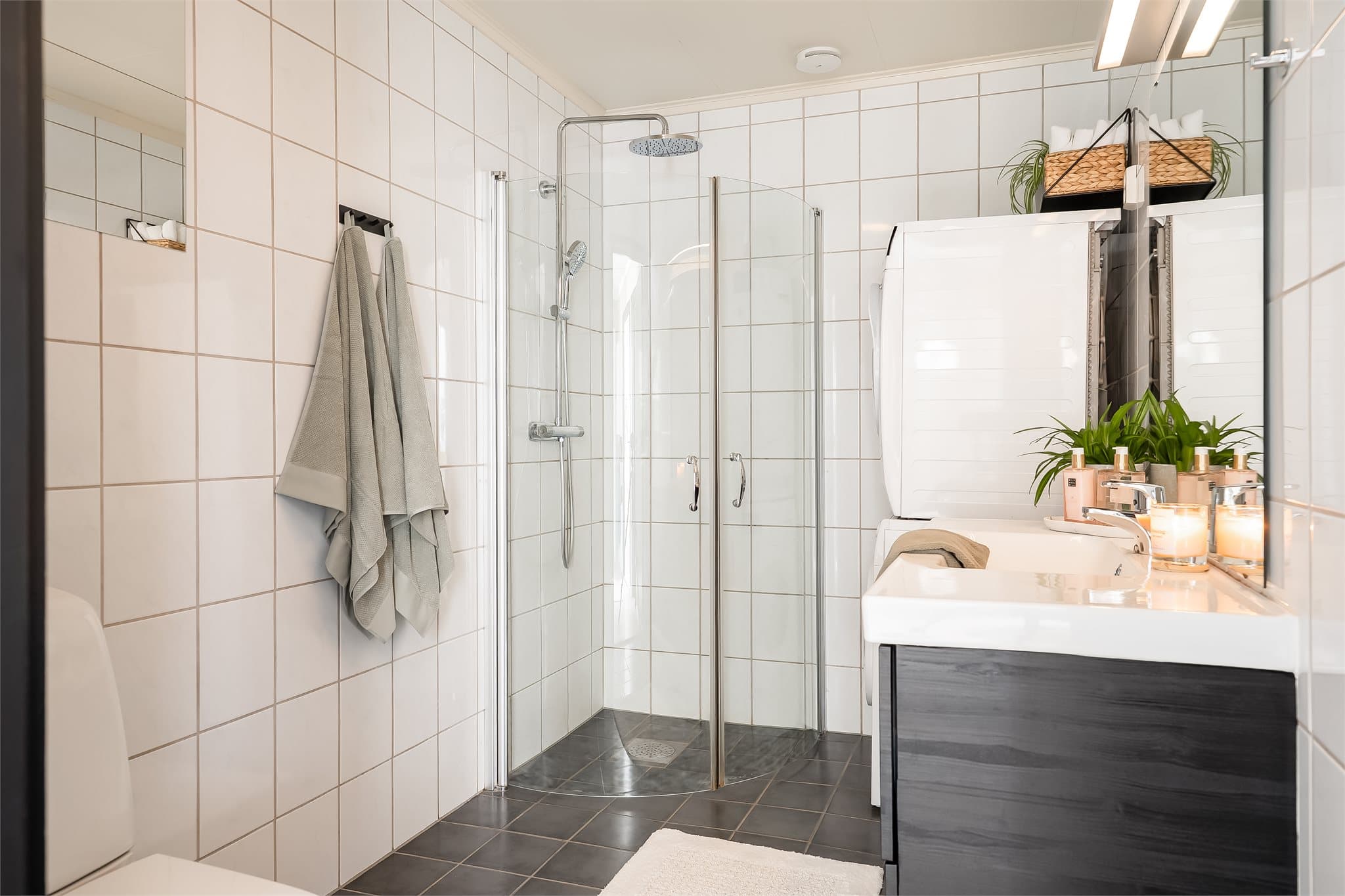 Lyst baderom utstyrt med dusjhjørne med innfellbare dusjdører, servantinnredning og toalett.