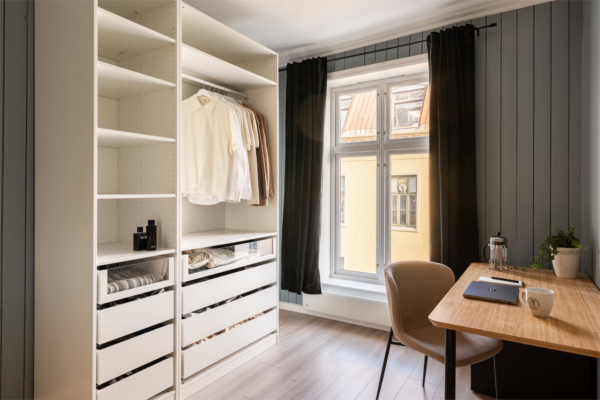 Langs den ene veggen er det etablert en åpen garderobeløsning med rikelig oppbevaringsplass i hyller, skuffer og heng.