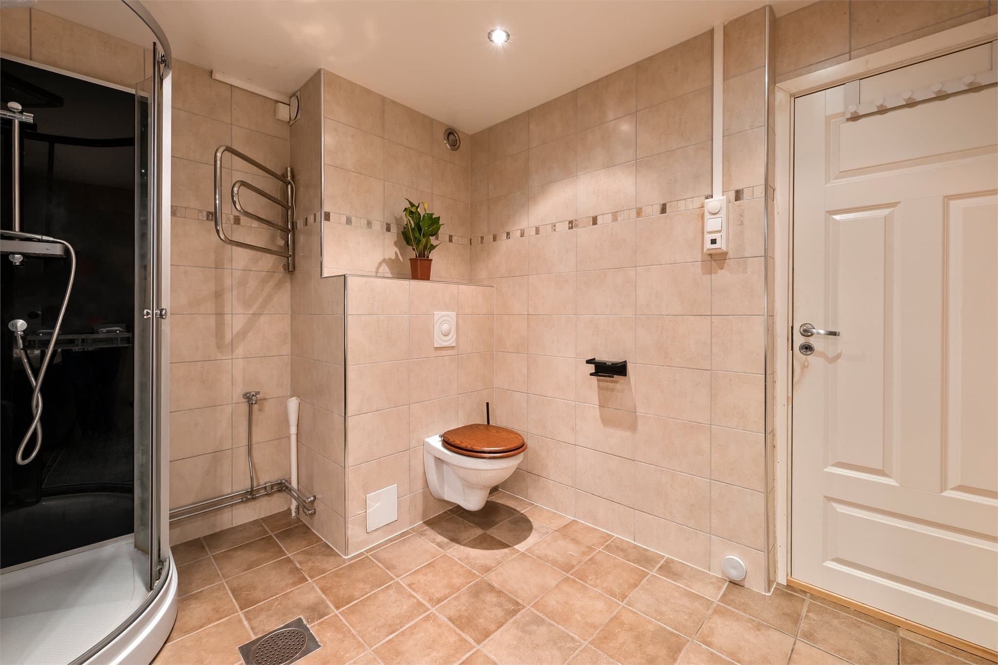 Badet er utstyrt med servantskap, dusjkabinett, vegghengt toalett og håndkletørker.