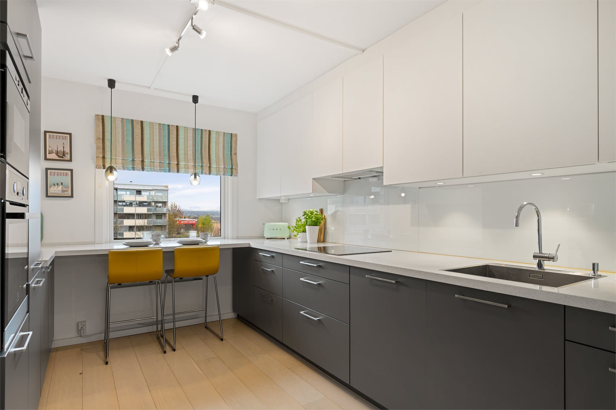Kjøkkenet fra Schmidt har et moderne og tidløst uttrykk med slette fronter i hvitt og grått, kombinert med en elegant laminat benkeplate i steinimitasjon. Den praktiske U-formen gir svært gode arbeidsflater og rikelig med skapplass.
