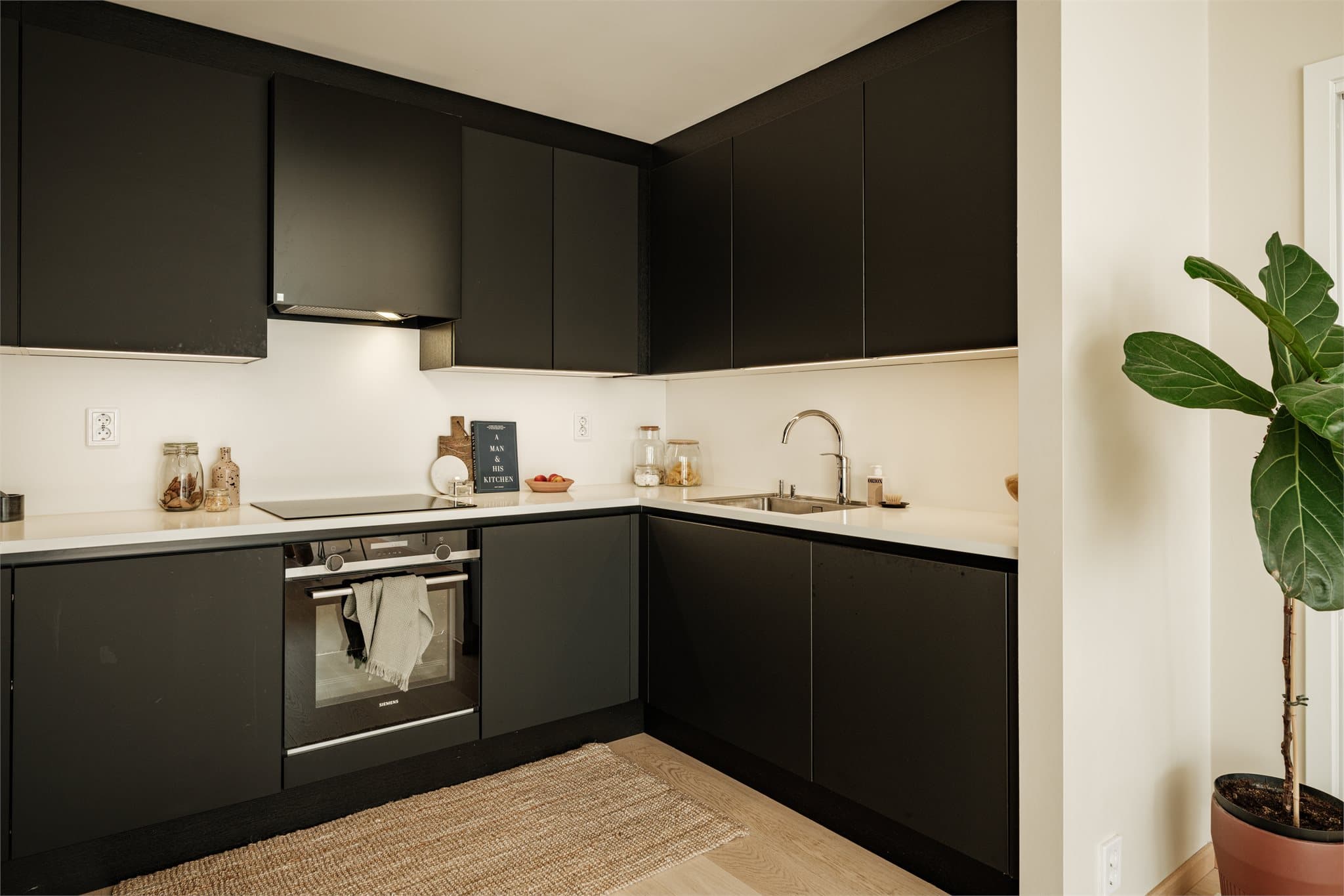 Stilrent kjøkken med integrerte hvitevarer som oppvaskmaskin, stekeovn, induksjon koketopp og kjøl-/fryseskap.