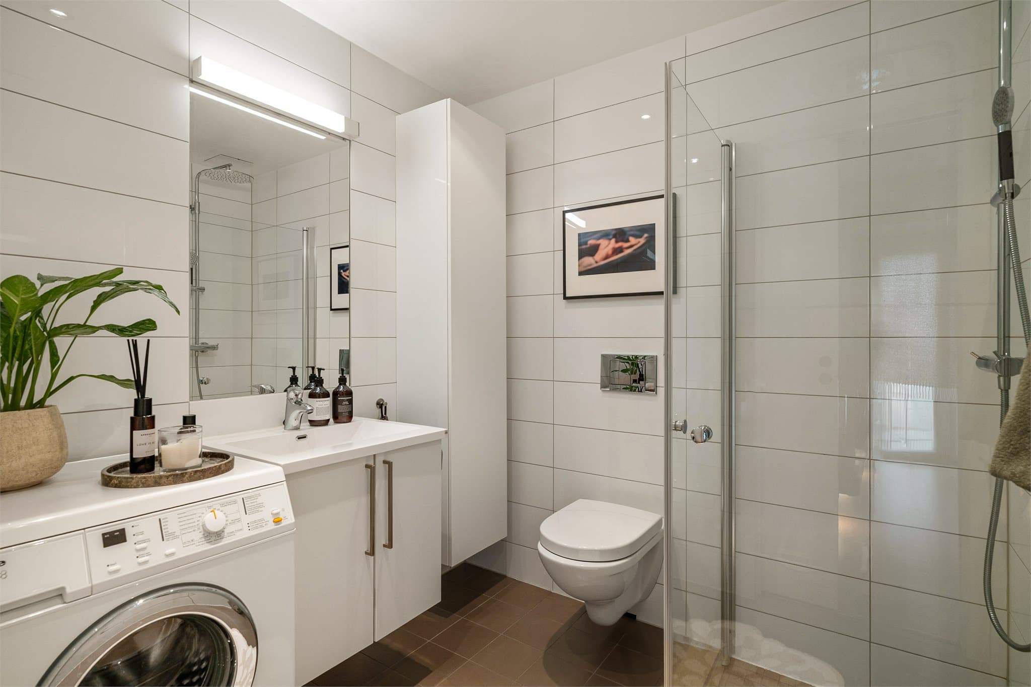 Stilrent bad med vegghengt toalett og et praktisk dusjhjørne med innfellbare glassdører. Badet har opplegg for vaskemaskin.