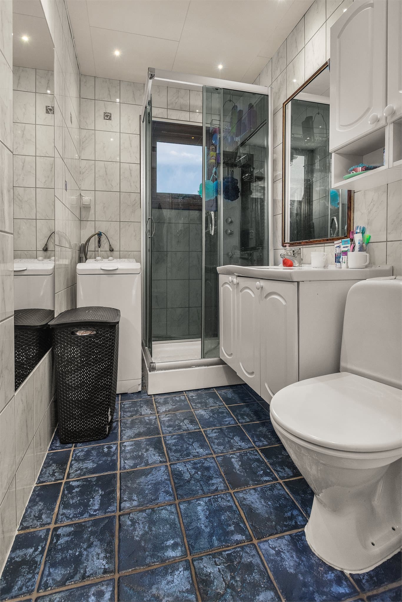 Badet i andre etasje har flislagte vegger og gulv med varmekabler, dusjkabinett og opplegg for vaskemaskin.