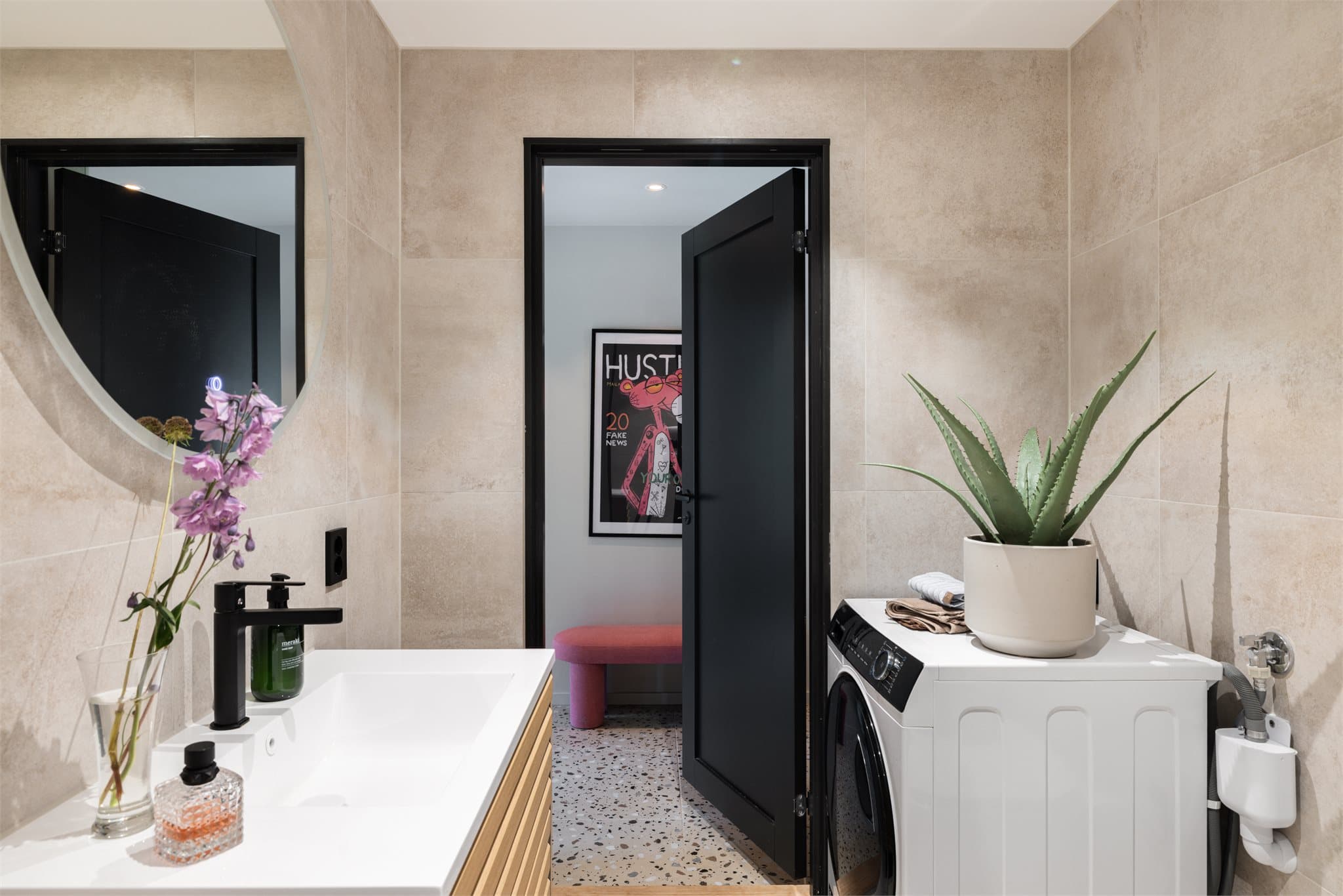 Moderne flislagt bad med dusjnisje og glassvegg, servant med ettgreps blandebatteri, vegghengt toalett og opplegg for vaskemaskin.