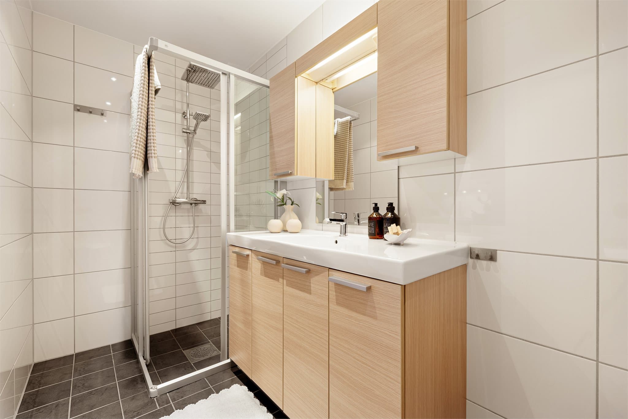 Badet er utstyrt med dusjhjørne, stor servantinnredning, vegghengt toalett og opplegg for vaskemaskin.