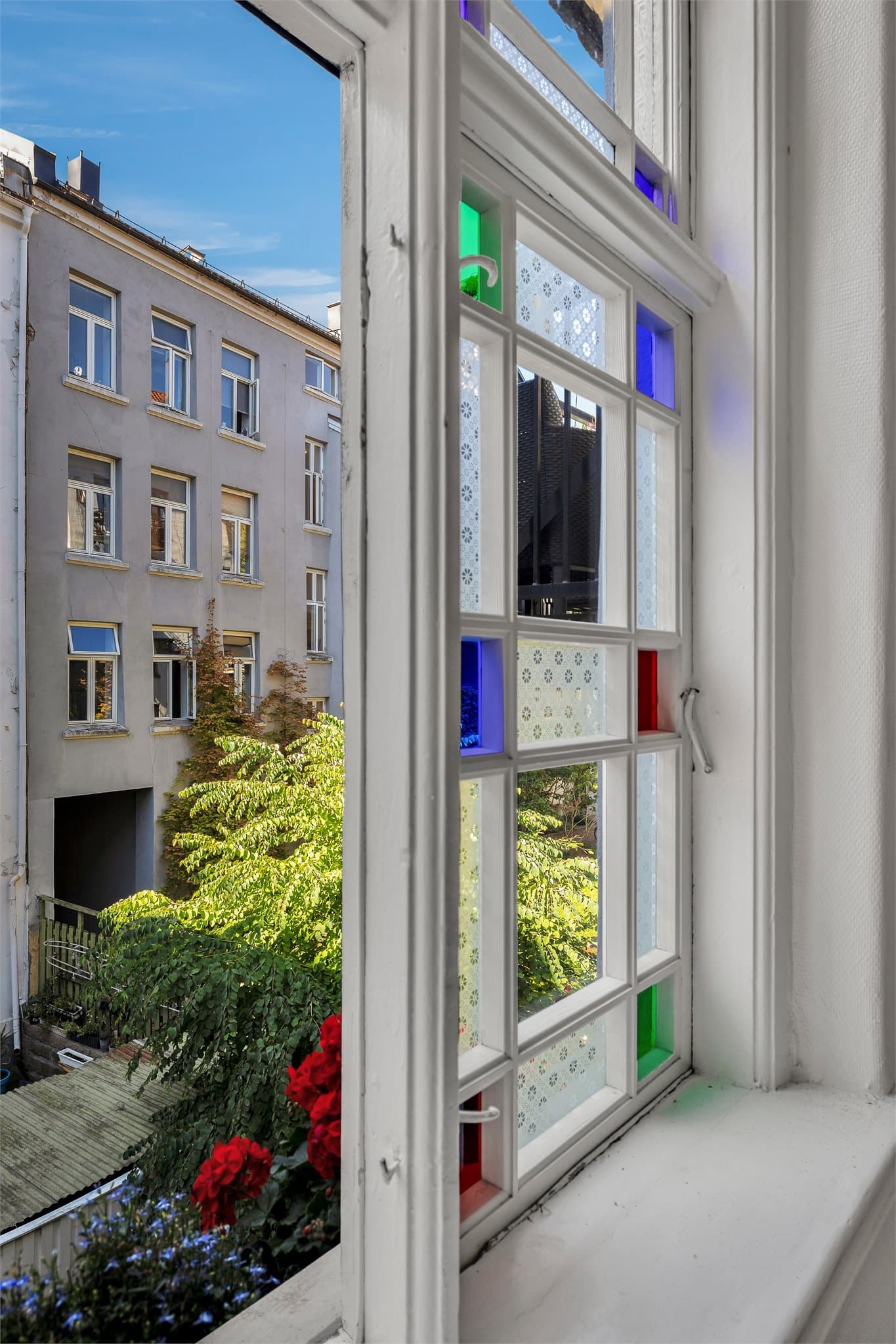 Sommerbilde tatt fra vinduet i trappeoppgangen med utsyn til grønne og frodige omgivelser.