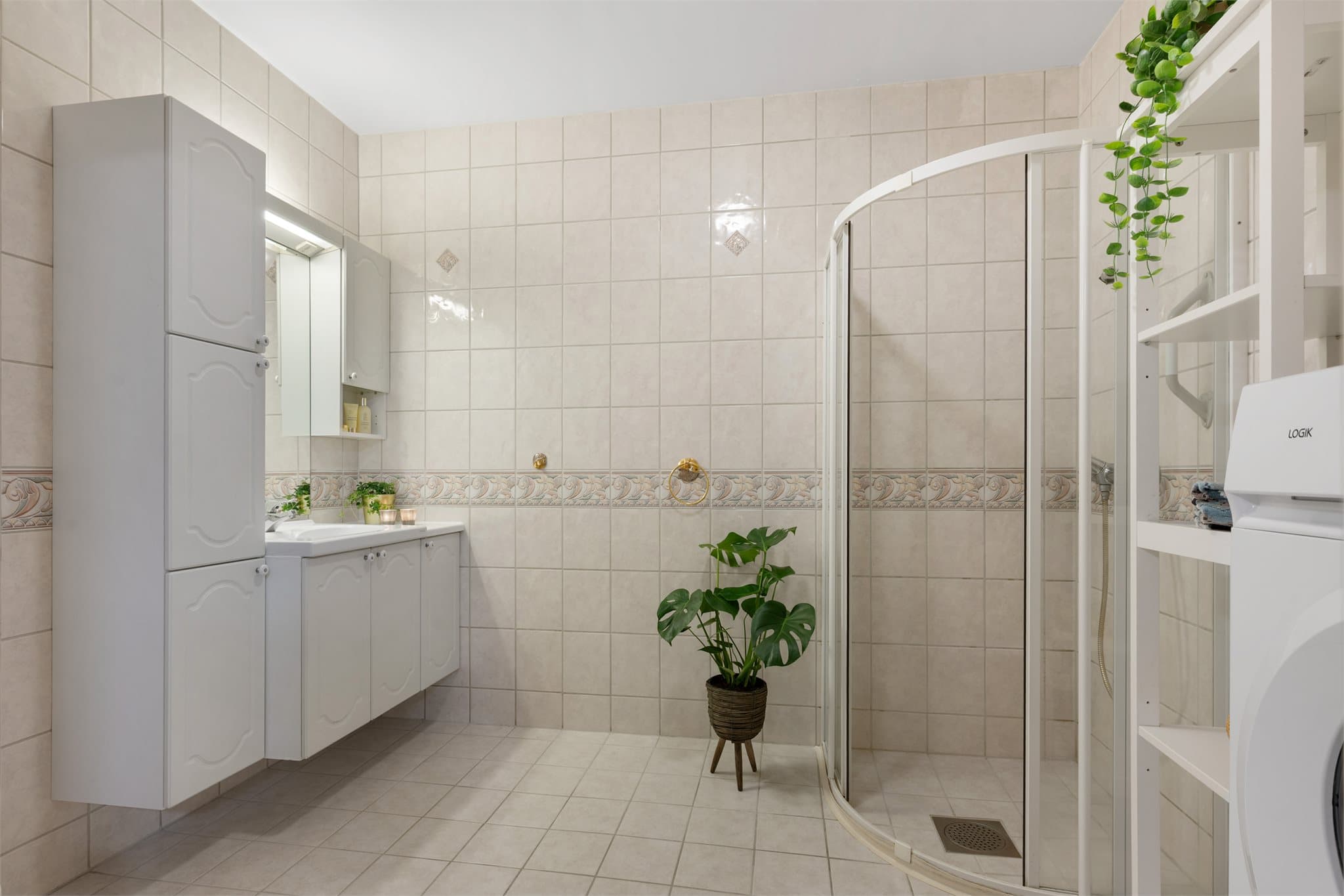 Flislagt baderom av god størrelse med dusjhjørne med skyvedører i herdet glass, rikelig med skapplass i baderomsinnredning, klosett og opplegg for vaskemaskin.