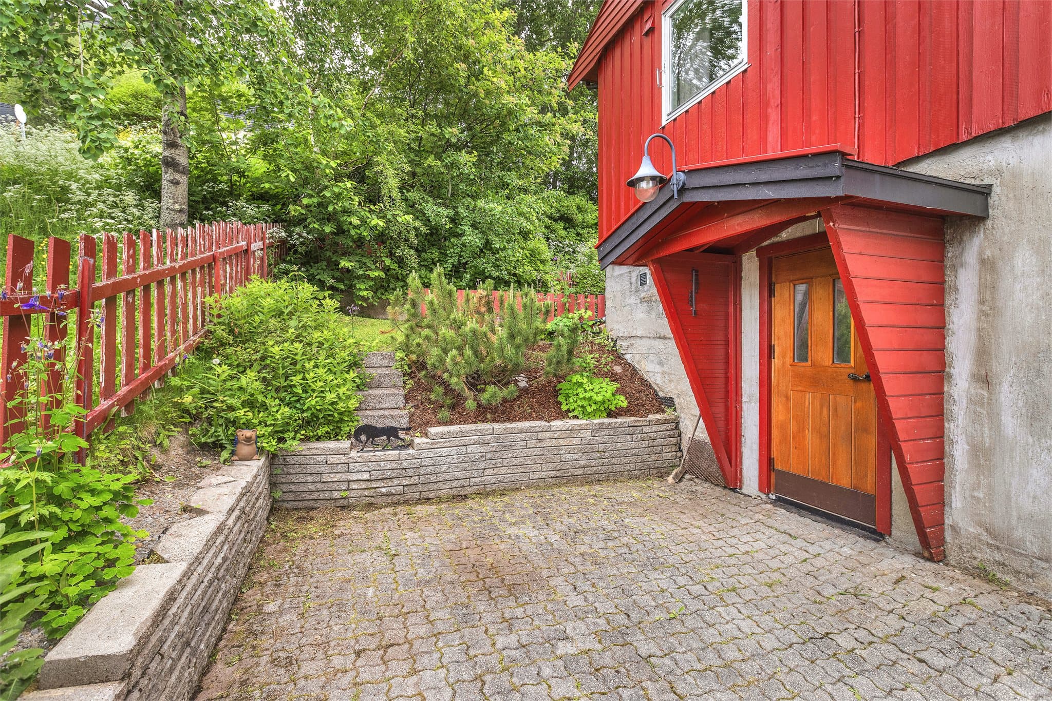 Overbygget inngangsparti til underetasjen, med belegningsstein på uteplassen.