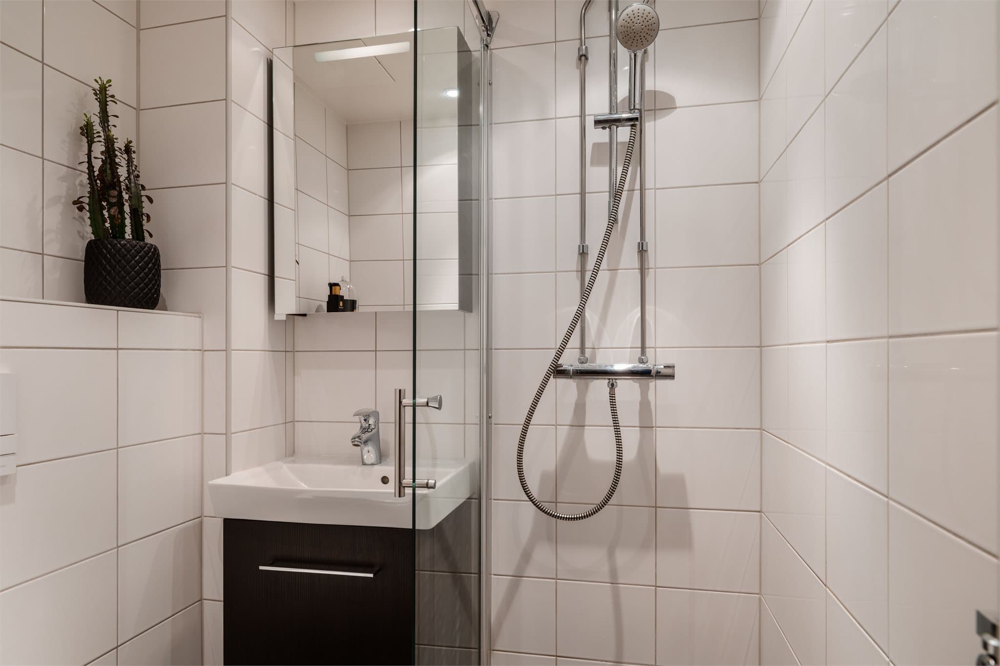 Innredningen består av servant med underskap, speilskap, veggfestet toalett og dusj.