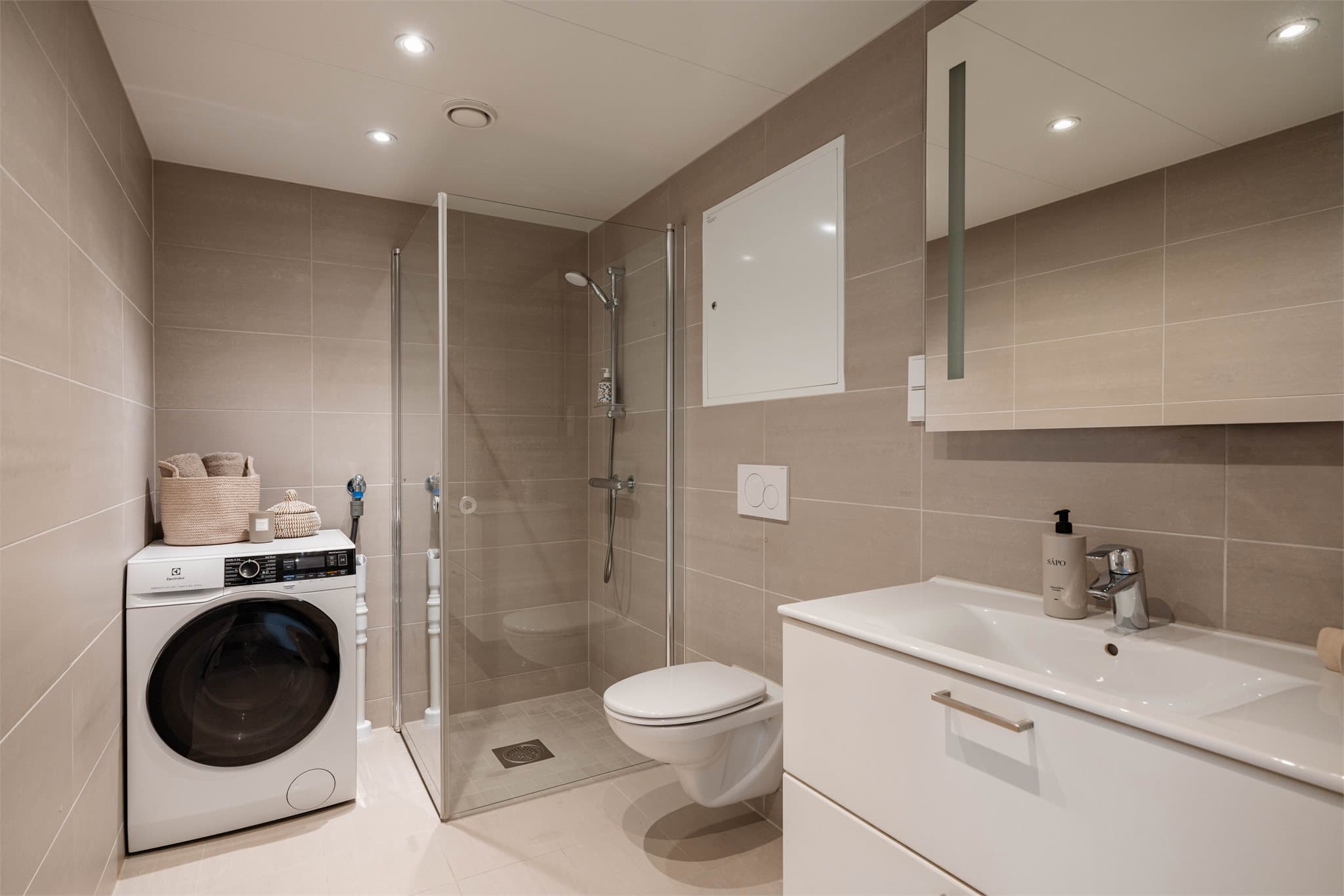 Delikat flislagt bad med elektrisk gulvvarme, dusjhjørne med svingbare glassdører og opplegg for vaskemaskin.