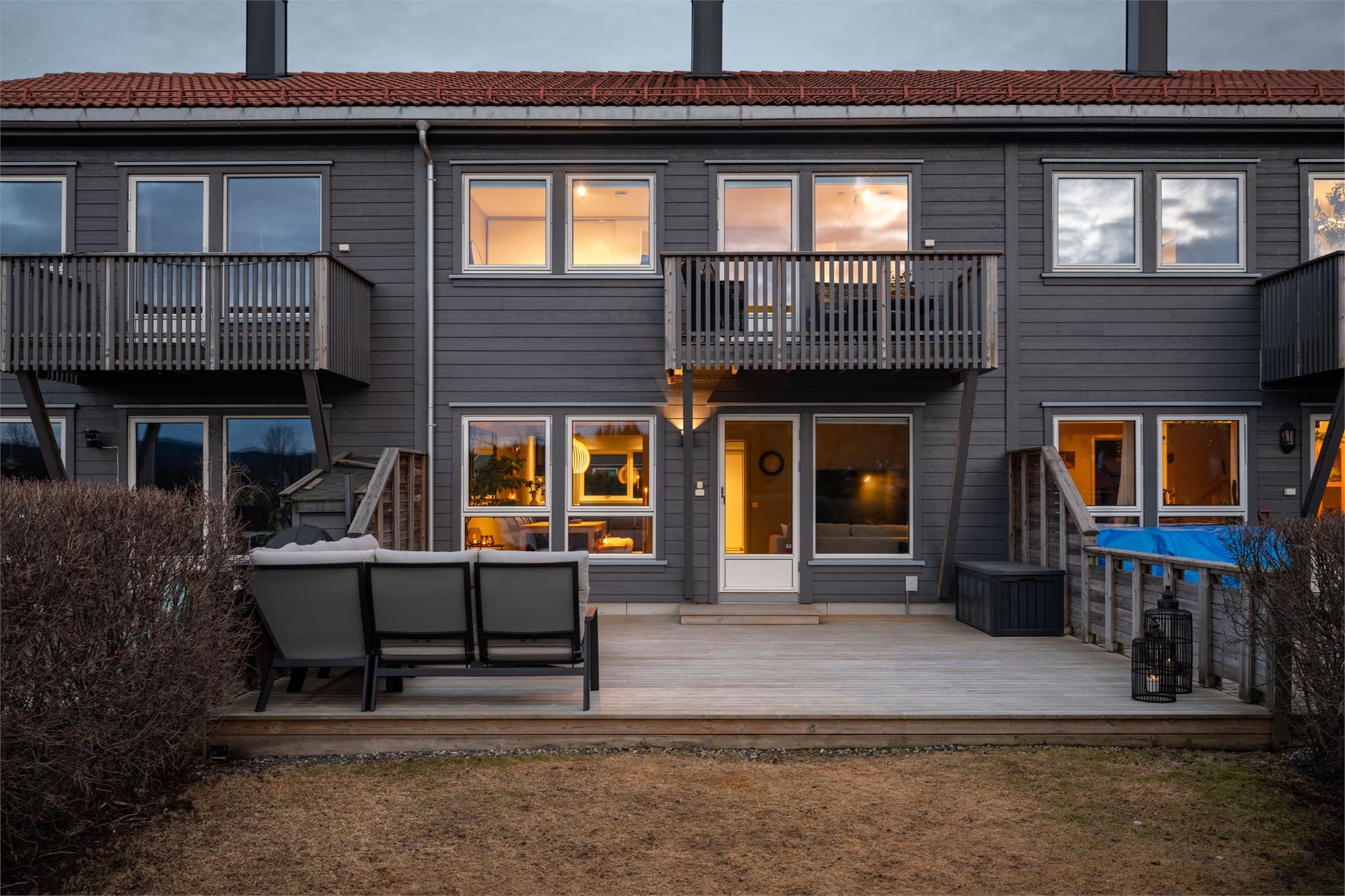 Fasaden mot hagen på kveldstid, med lys fra de store vindusflatene.