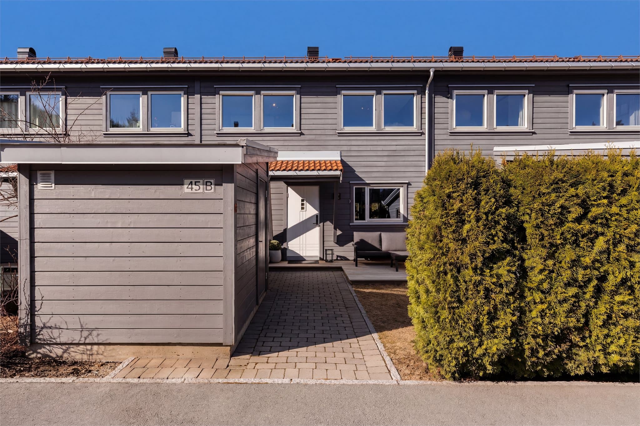 Rekkehuset har en pen og velholdt fasade med panelkledning og takstein fra byggeåret 2012. To uteboder med god lagringsplass.