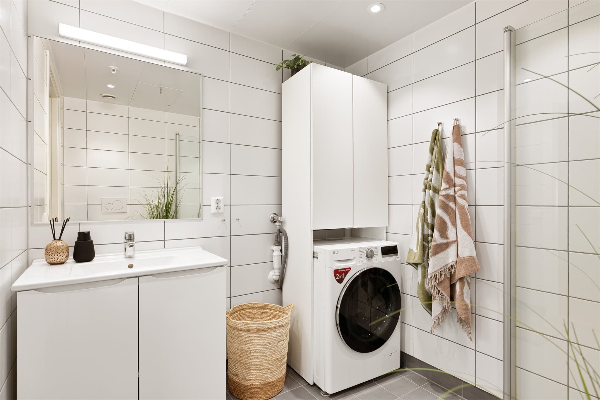 Badet har vegghengt toalett, dusjhjørne, servantinnredning og opplegg for vaskemaskin.