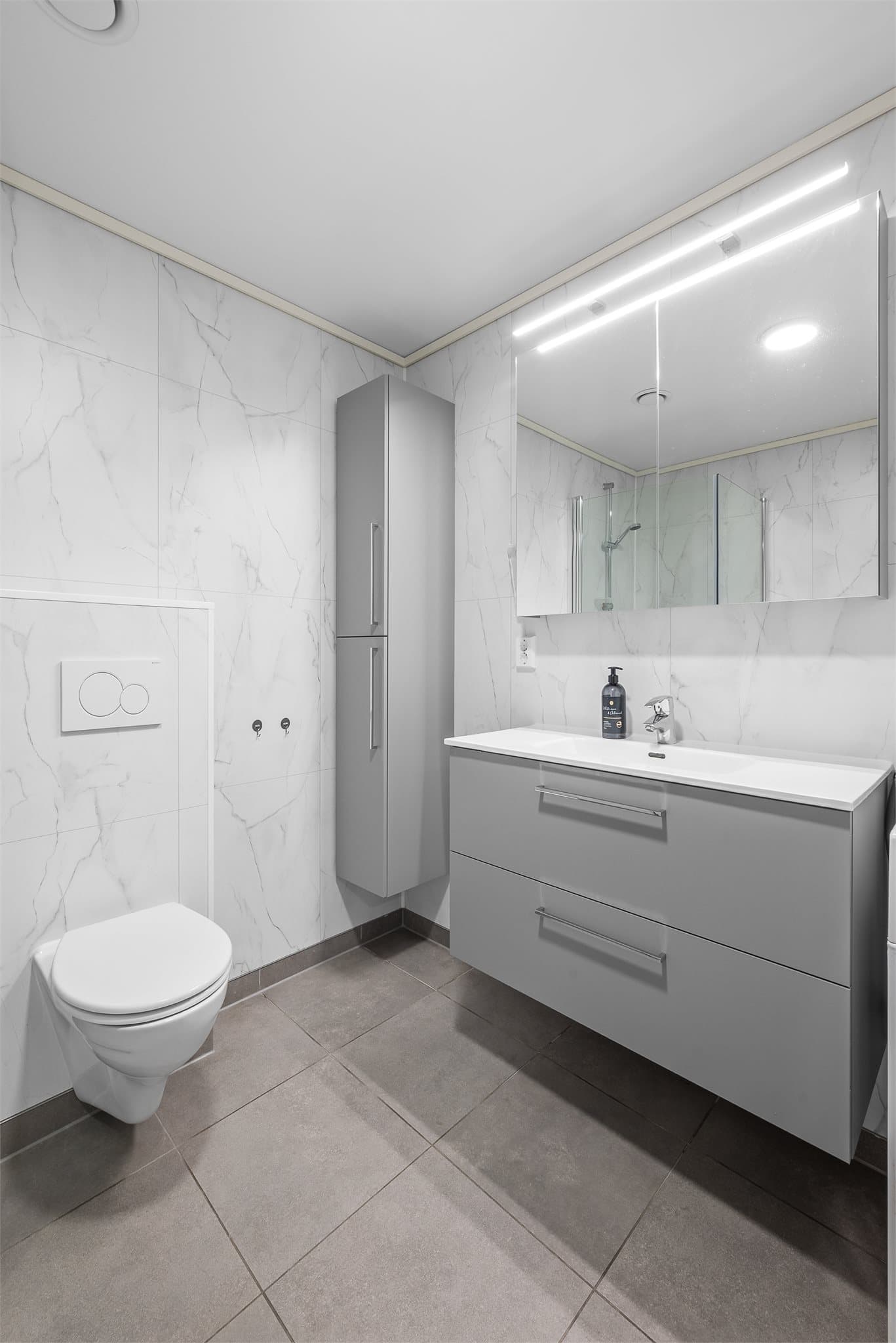 Moderne fargetoner og god belysning fra både tak og speil gir badet et stilrent og innbydende uttrykk.
