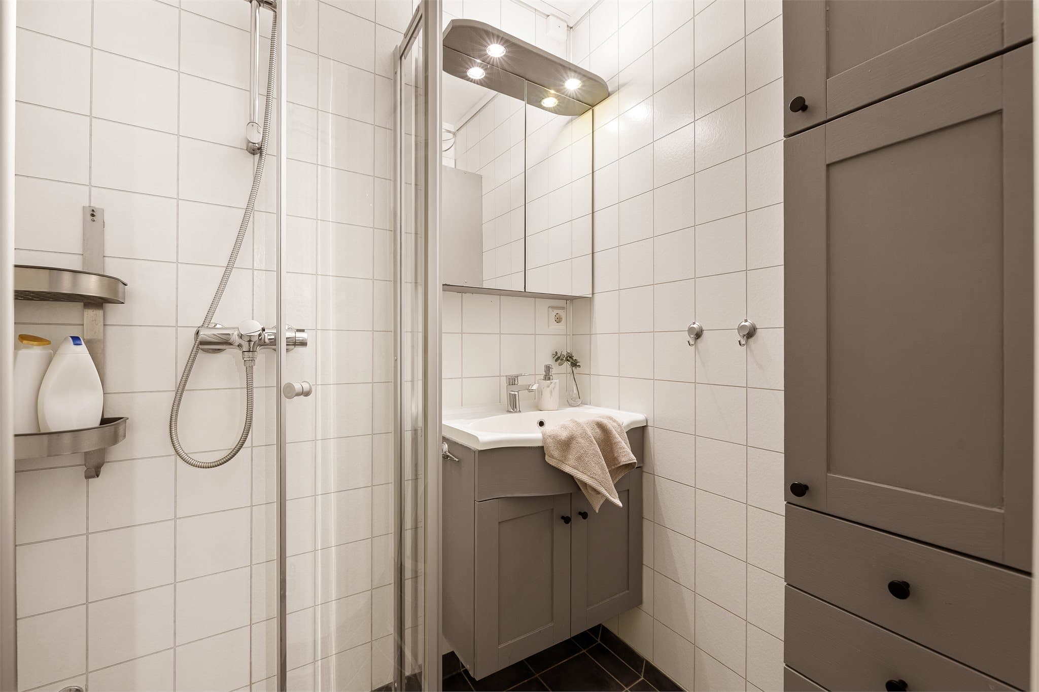 Flislagt bad utstyrt med dusjhjørne, servant og speilskap med integrert belysning.