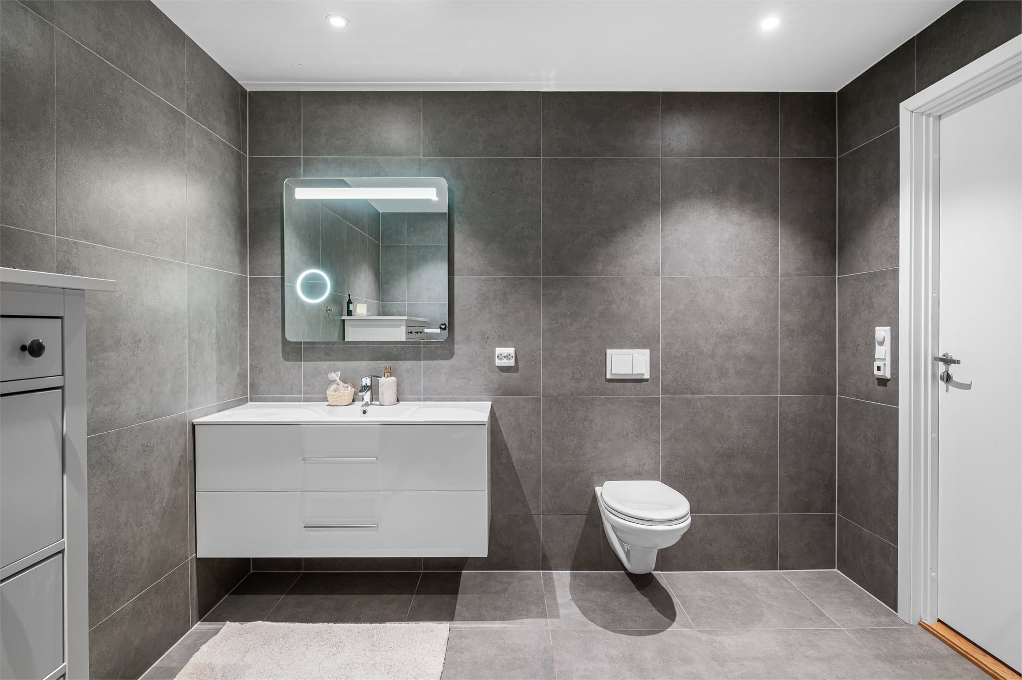 - Badet er innredet med vegghengt toalett, heldekkende servant og dusjdører i glass -