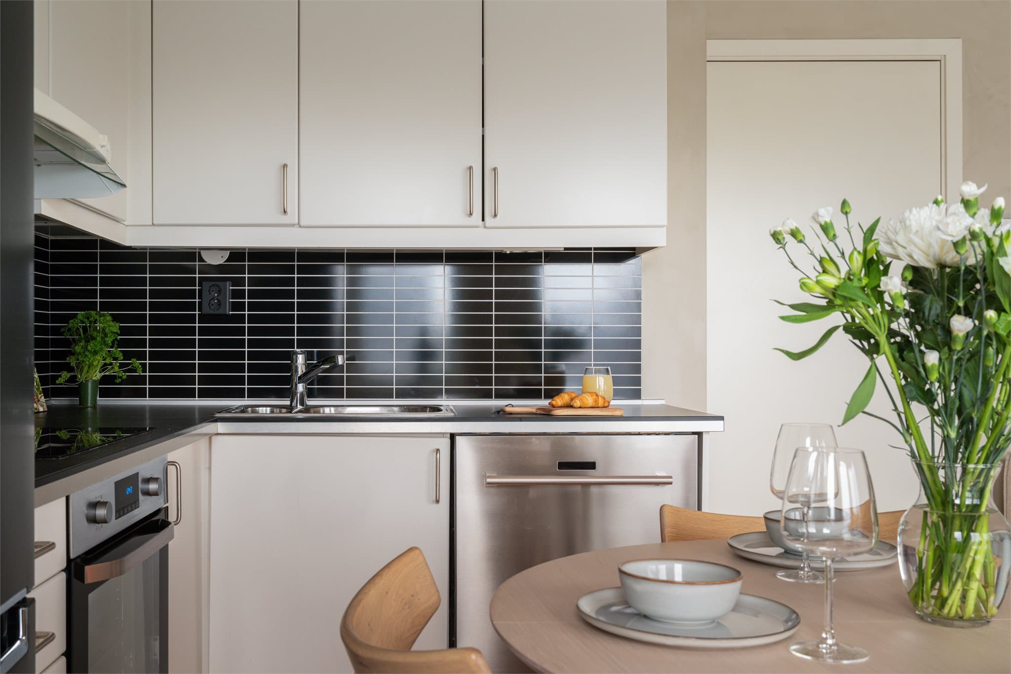 Det er flislignende plater på vegg over benkeplate og belysning via lysstoffrør under overskap.