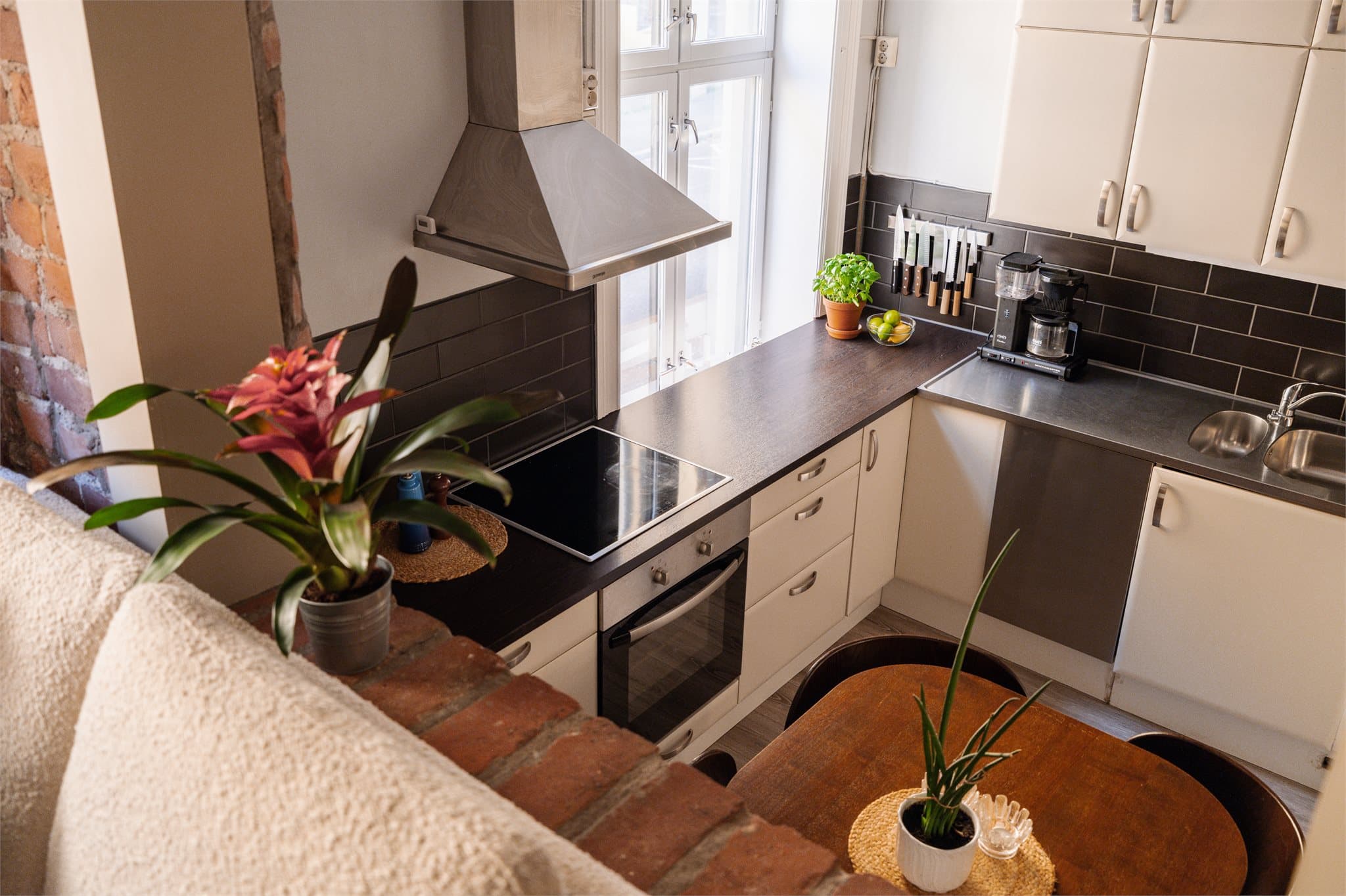 Kjøkkenet har en funksjonell og tidløs utforming med glatte, fabrikklakkerte fronter og laminert benkeplate med nedfelt, heldekkende kum i rustfritt stål. Over benkeplaten er det lagt fliser, og belysningen ivaretas av lystoffrør montert under overskapene