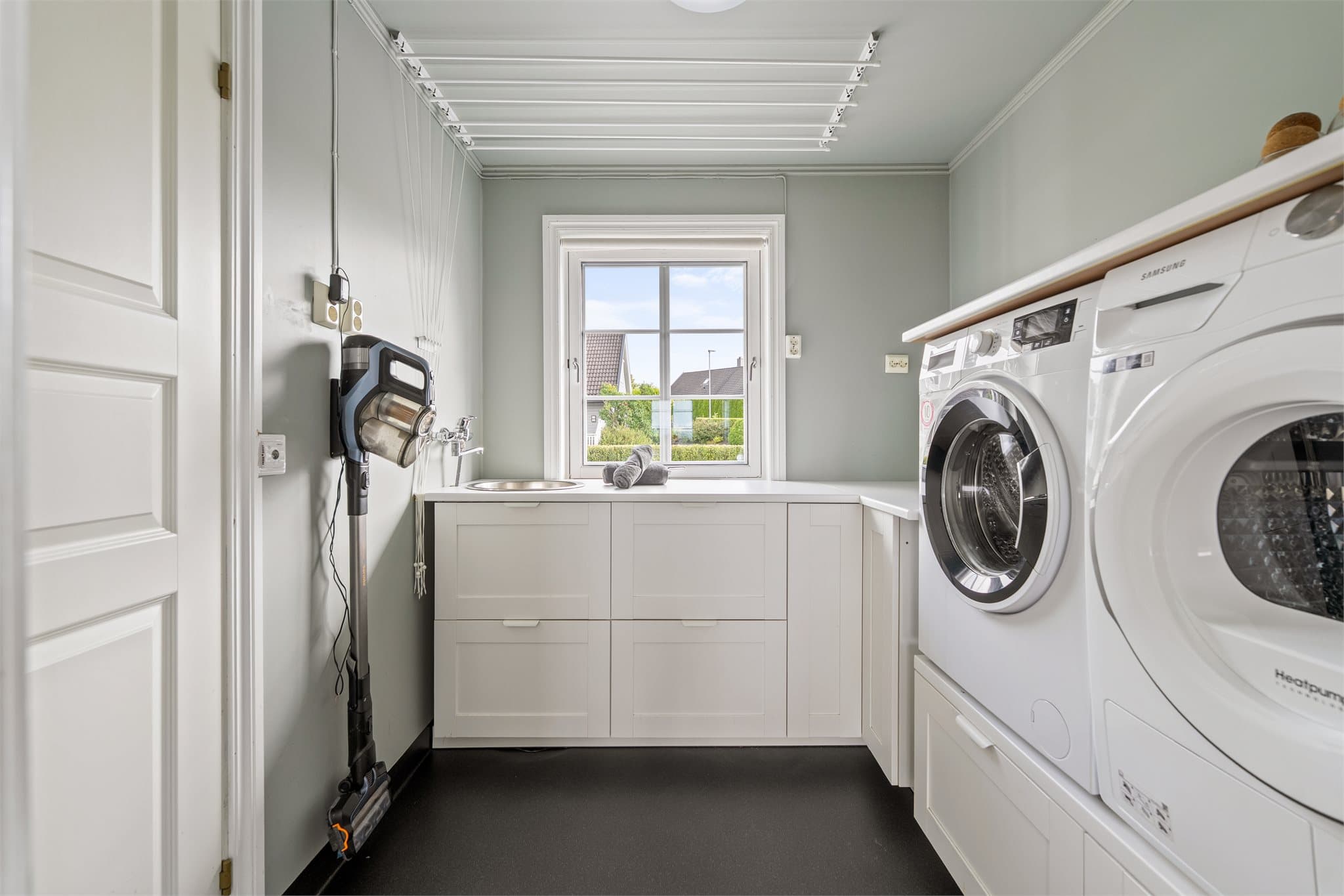 Vegg-i-vegg med kjøkkenet ligger det et praktisk vaskerom med lys innredning og opplegg for vaskemaskin og tørketrommel.