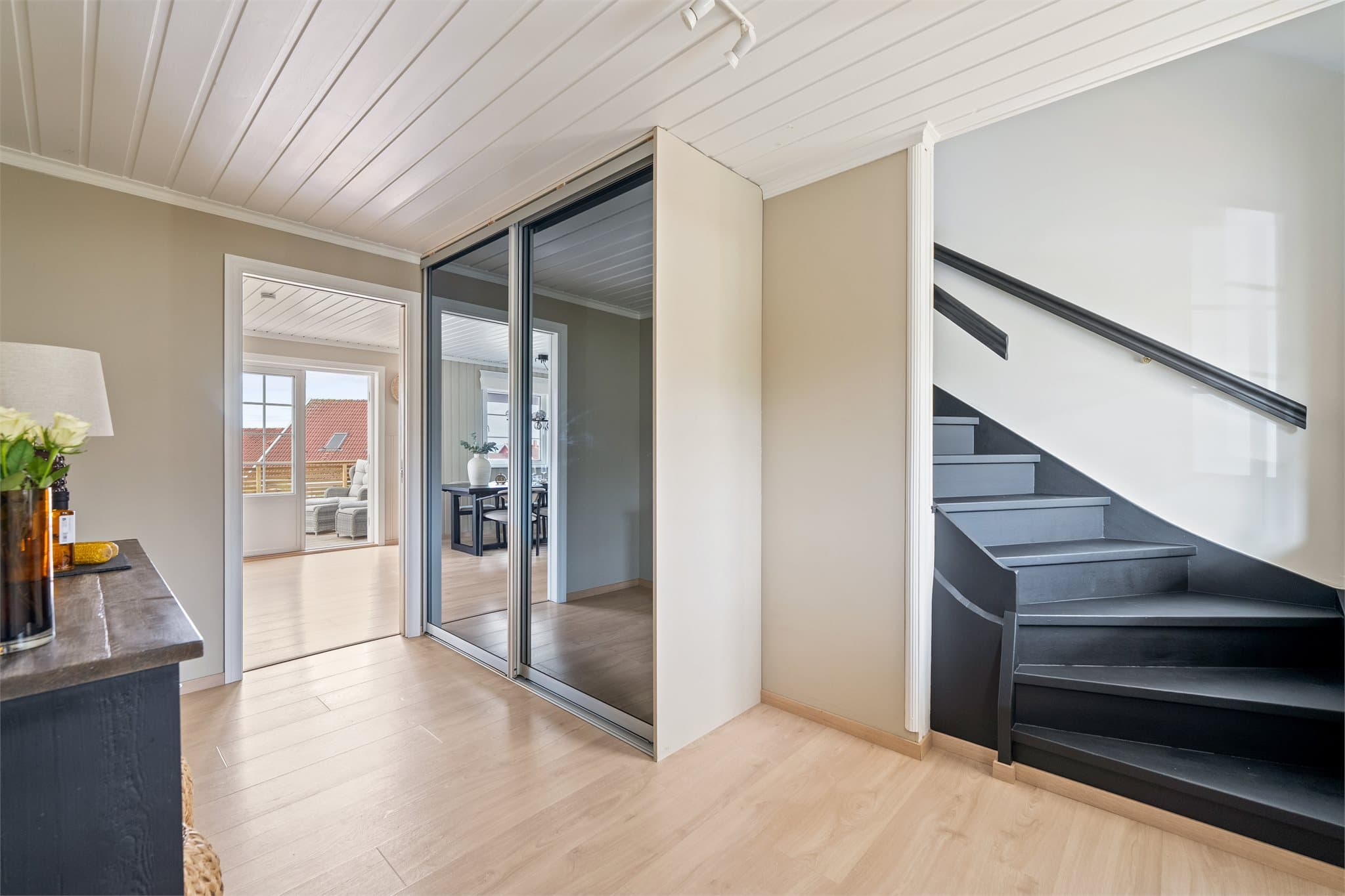 Her er det god plass til oppbevaring i en praktisk skyvedørsgarderobe med speildører, som både gir rommet et luftig uttrykk og bidrar til funksjonell lagring av yttertøy og sko.